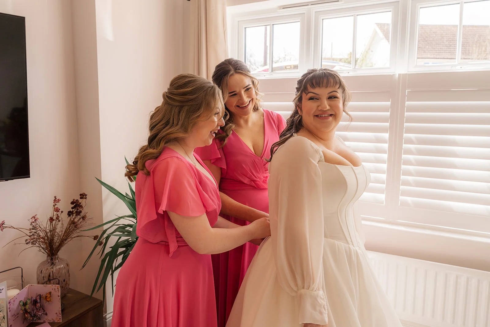 Emily smiles while getting ready with her bridesmaids before the wedding ceremony at Coombe Lodge in Somerset, UK, as they help with the finishing touches to her dress.