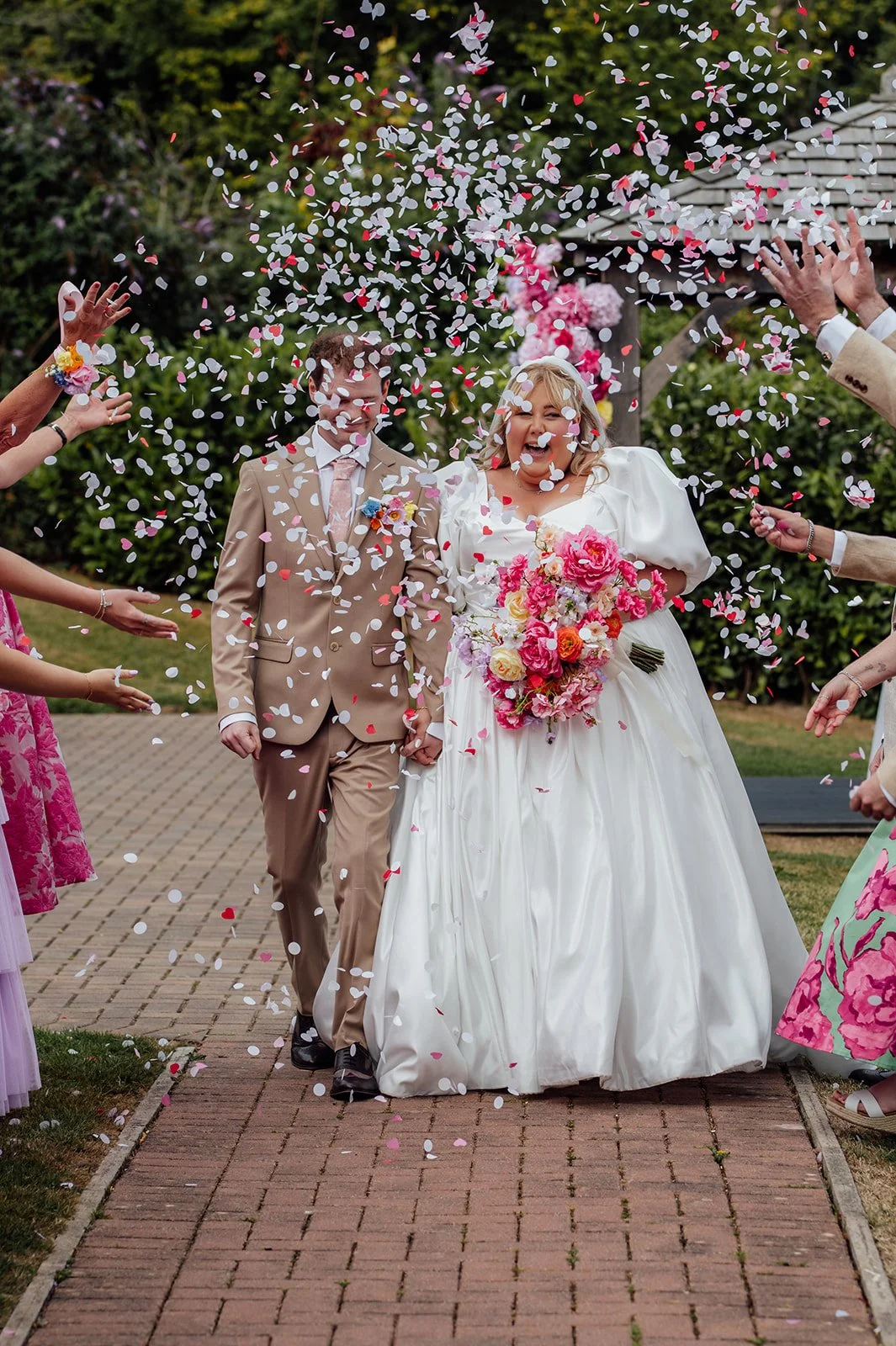 Holly & Alex walk through a shower of pink and white confetti after their ceremony at Sandy Cove Hotel in North Devon, photographed by Just James Weddings.