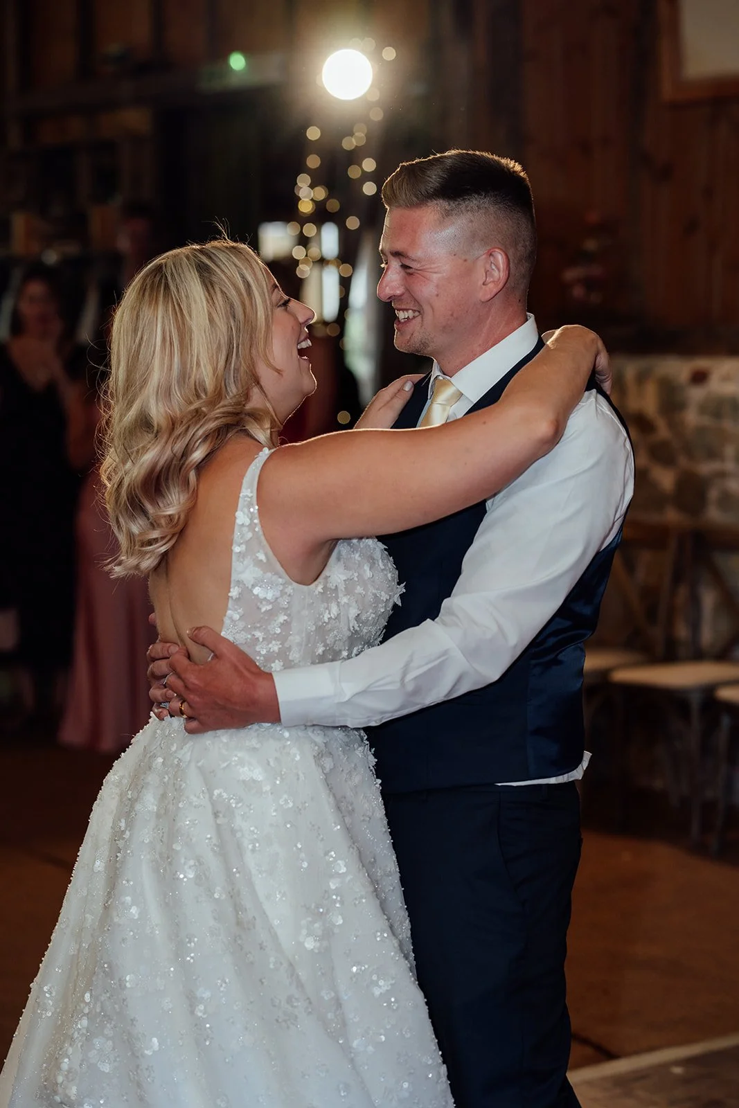 Elise and Tom smiling at each other during their first dance inside Bowerchalke Barn in Wiltshire, photographed by Just James Weddings.