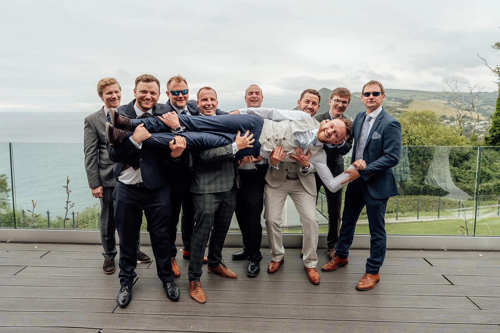 Connor’s wedding guests playfully lift him across their arms during a group photo on the terrace at Sandy Cove Hotel in North Devon, UK.