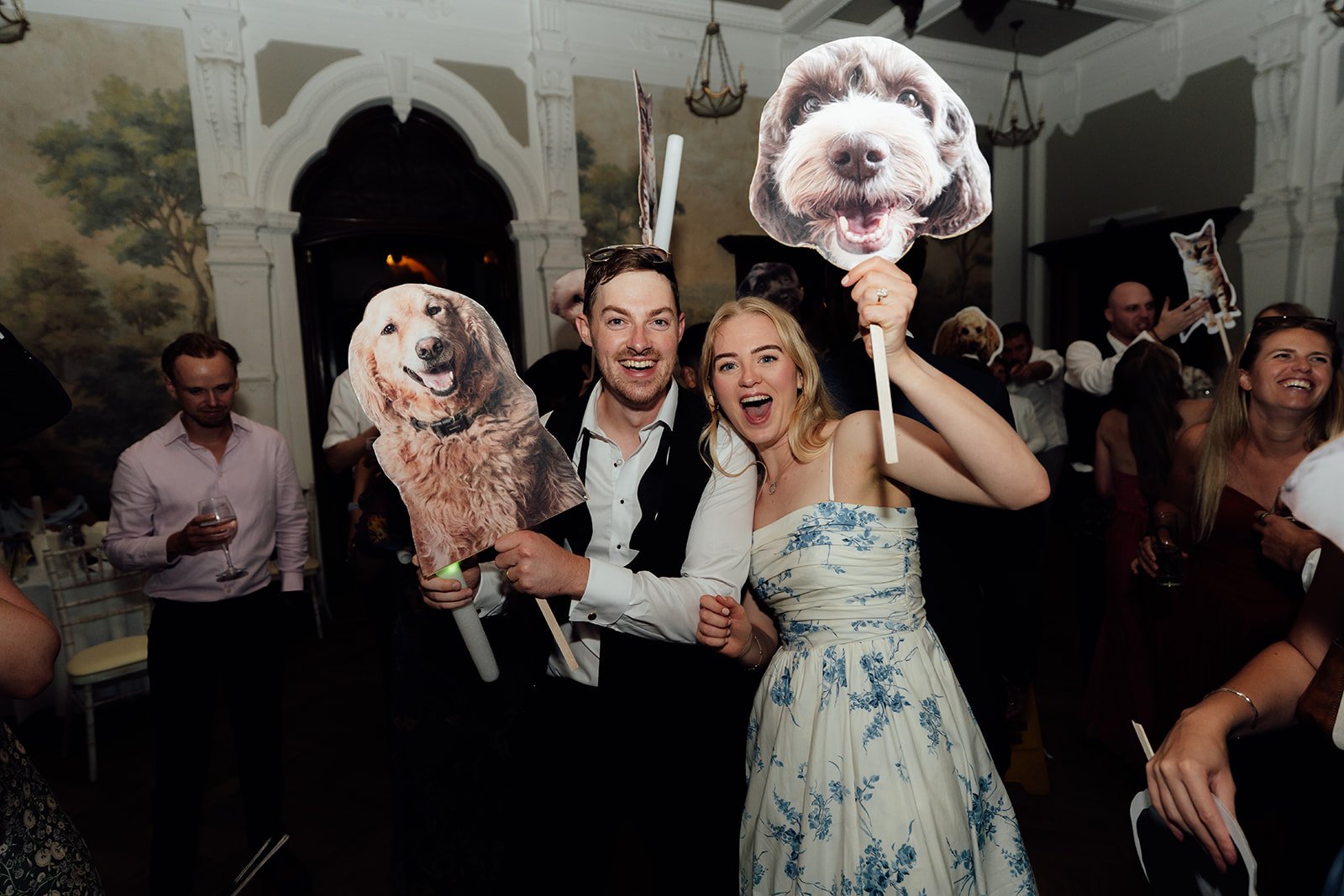 Caitlin and Kevin celebrating on the dance floor at Clevedon Hall in Somerset, holding playful cut-outs of their dogs as guests party around them.