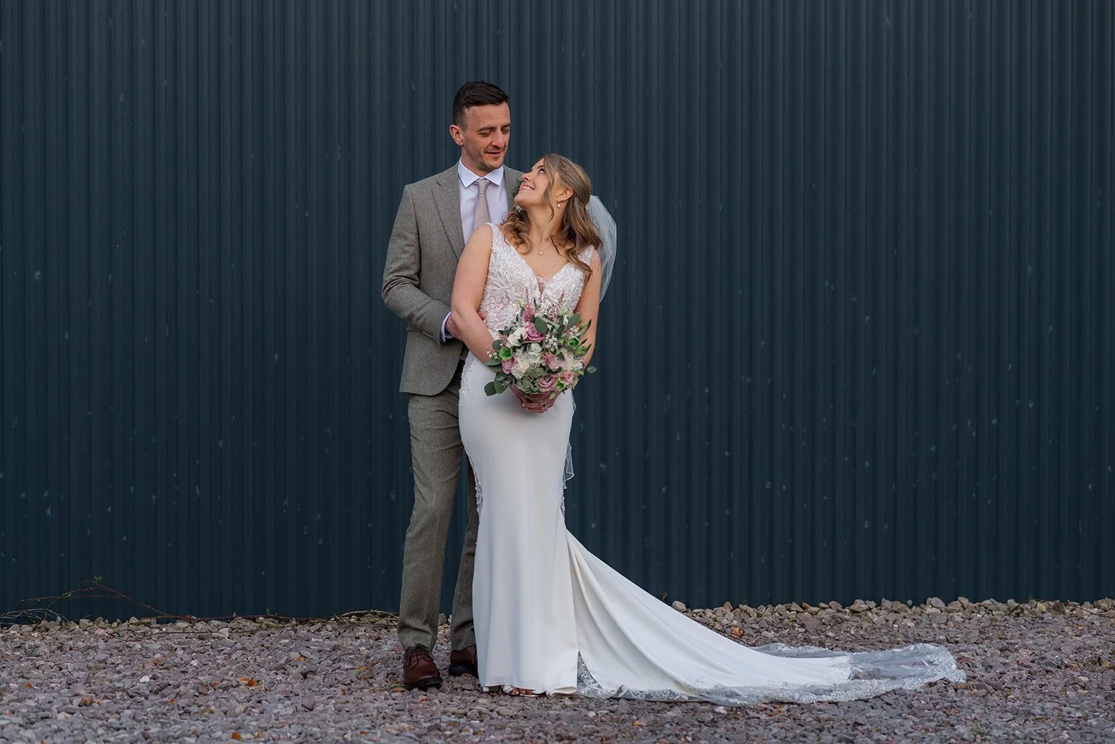Anna & Tom pose together against a dark barn wall during their wedding portraits at Winkworth Farm in the Cotswolds, photographed by Just James Weddings.