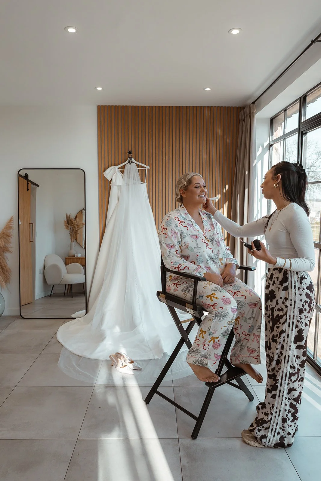 Jessie having her makeup applied during wedding morning preparations at Upton Barn & Walled Garden in Devon, UK. Her dress hangs nearby in soft natural light, capturing a calm, intimate moment before Jessie & Jay’s ceremony begins.