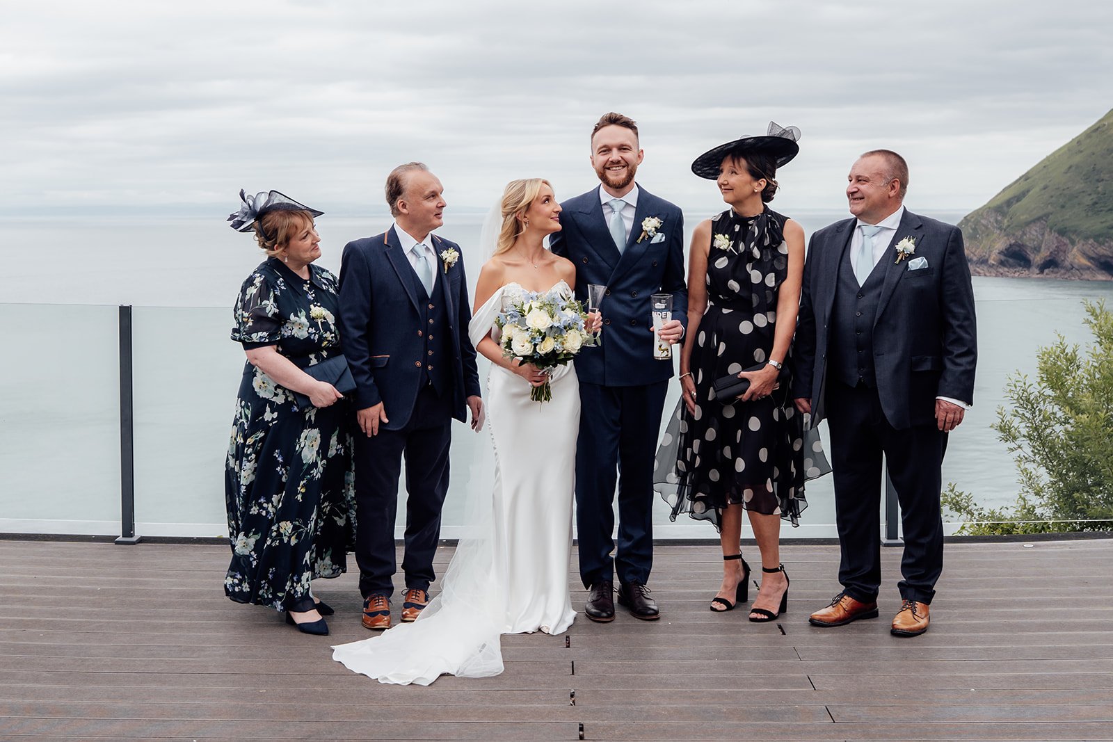 Amy & Connor pose with their parents during a relaxed family group portrait overlooking the sea at Sandy Cove Hotel in North Devon, UK.