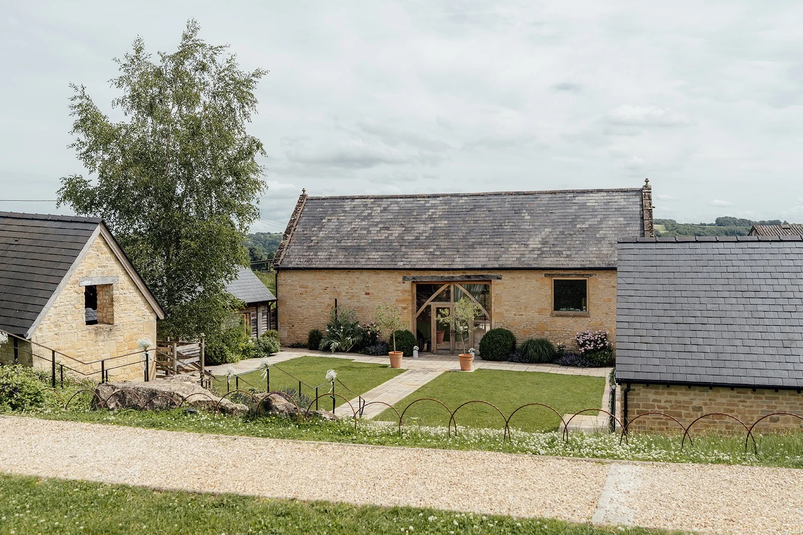 Exterior view of The Barn at Upcote in the Cotswolds, showing the stone barn buildings, courtyard and garden lawn, photographed by Just James Weddings.