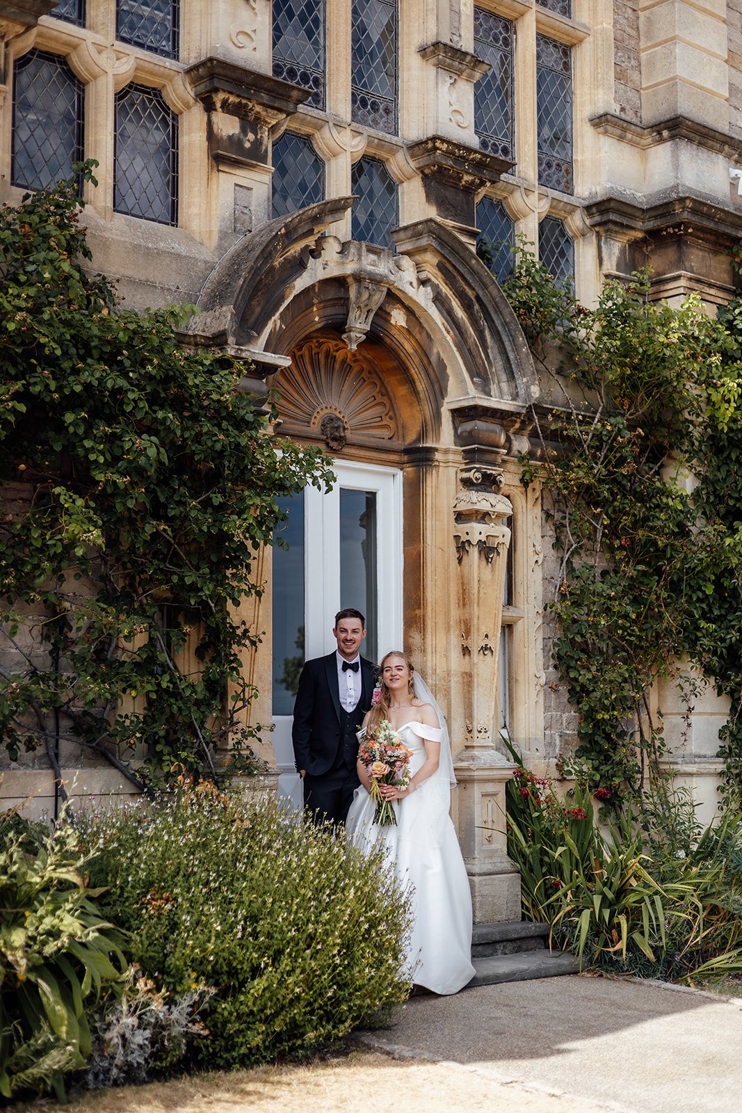 Caitlin & Kevin standing together beneath an ornate stone doorway at Clevedon Hall in Somerset, photographed by Just James Weddings.