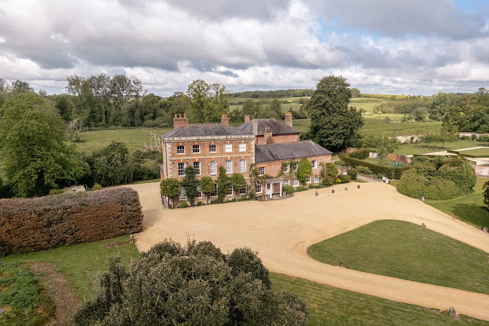Aerial view of Syrencot in Wiltshire, showing the historic house, gravel driveway, gardens and surrounding countryside, photographed by Just James Weddings for wedding venue inspiration.
