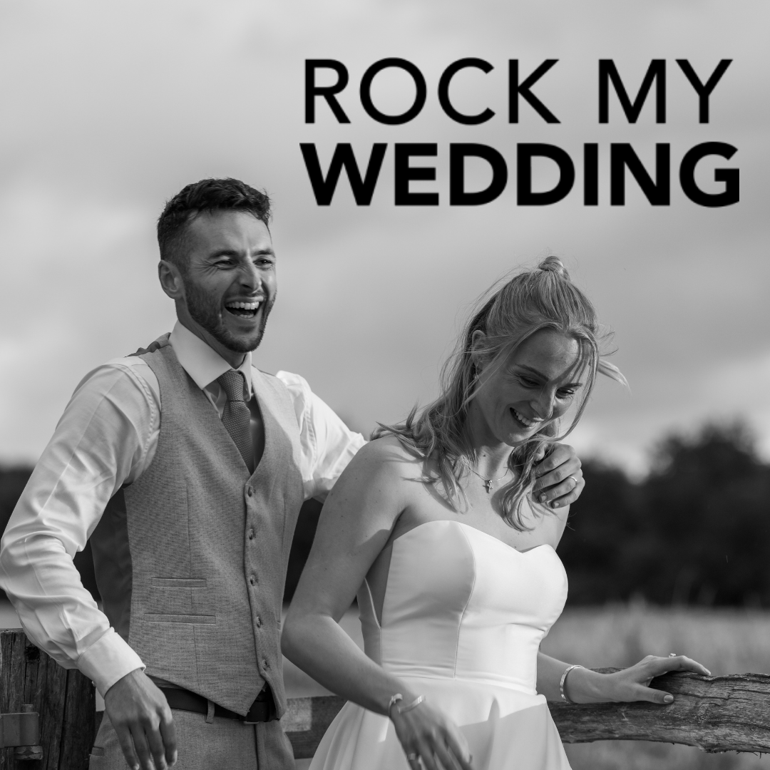 A black and white photo of a smiling bride in a strapless wedding dress and a groom in a vest and shirt, leaning on a wooden fence outdoors with trees in the background, with bold text that says "Rock My Wedding".