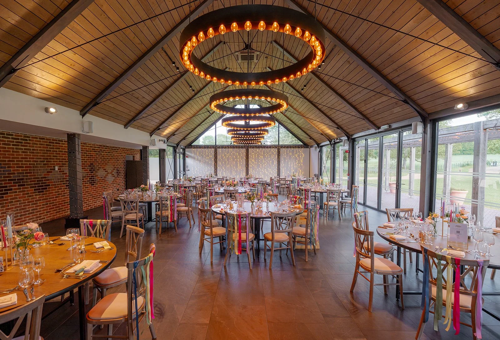 Wedding breakfast room at Syrencot in Wiltshire, with round tables, colourful ribbon details and circular pendant lights, photographed by Just James Weddings for reception venue inspiration.