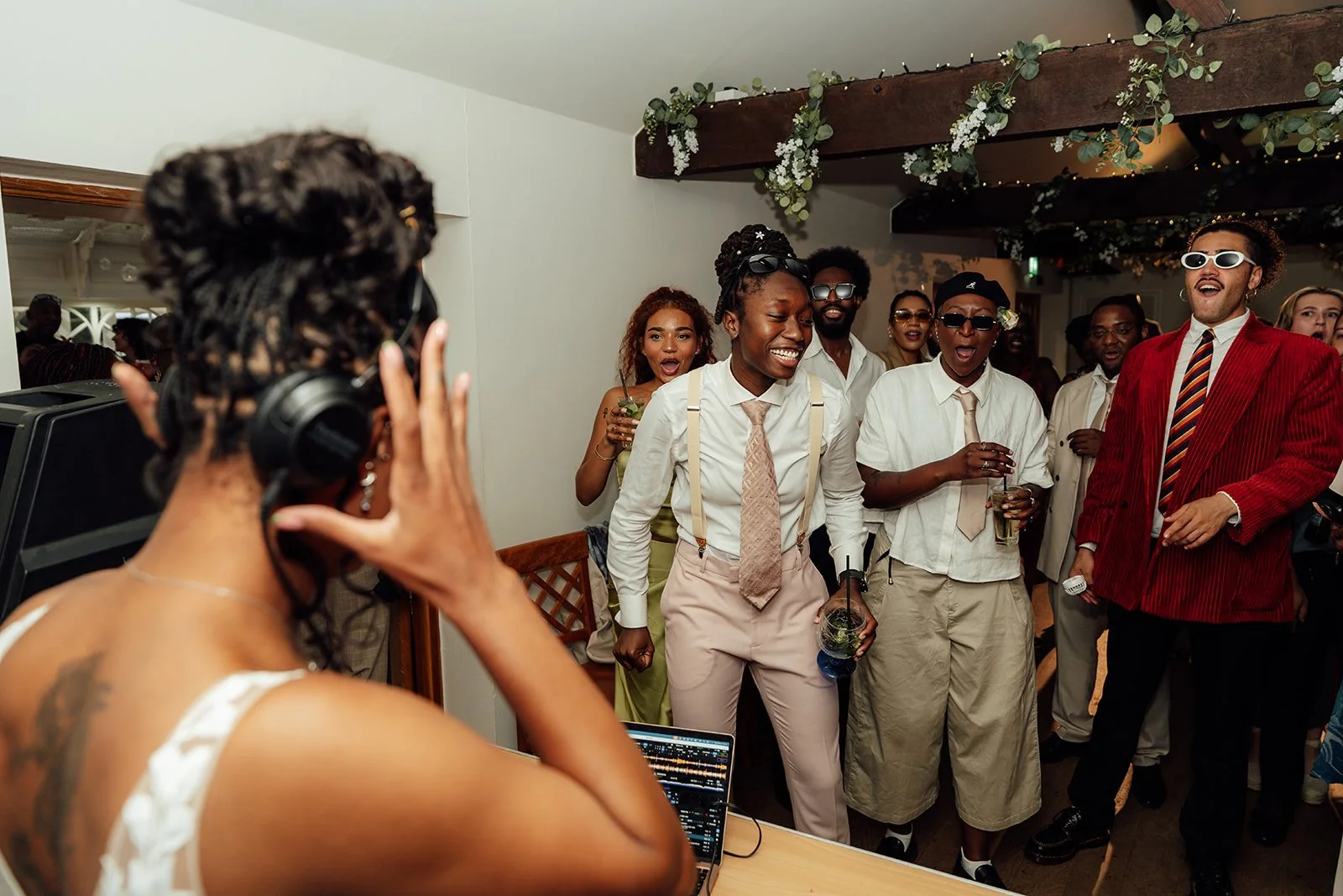 Larisha wearing headphones at the DJ booth as Kasey and their wedding guests laugh, sing and dance during the reception at Oaks Farm Weddings in Surrey.