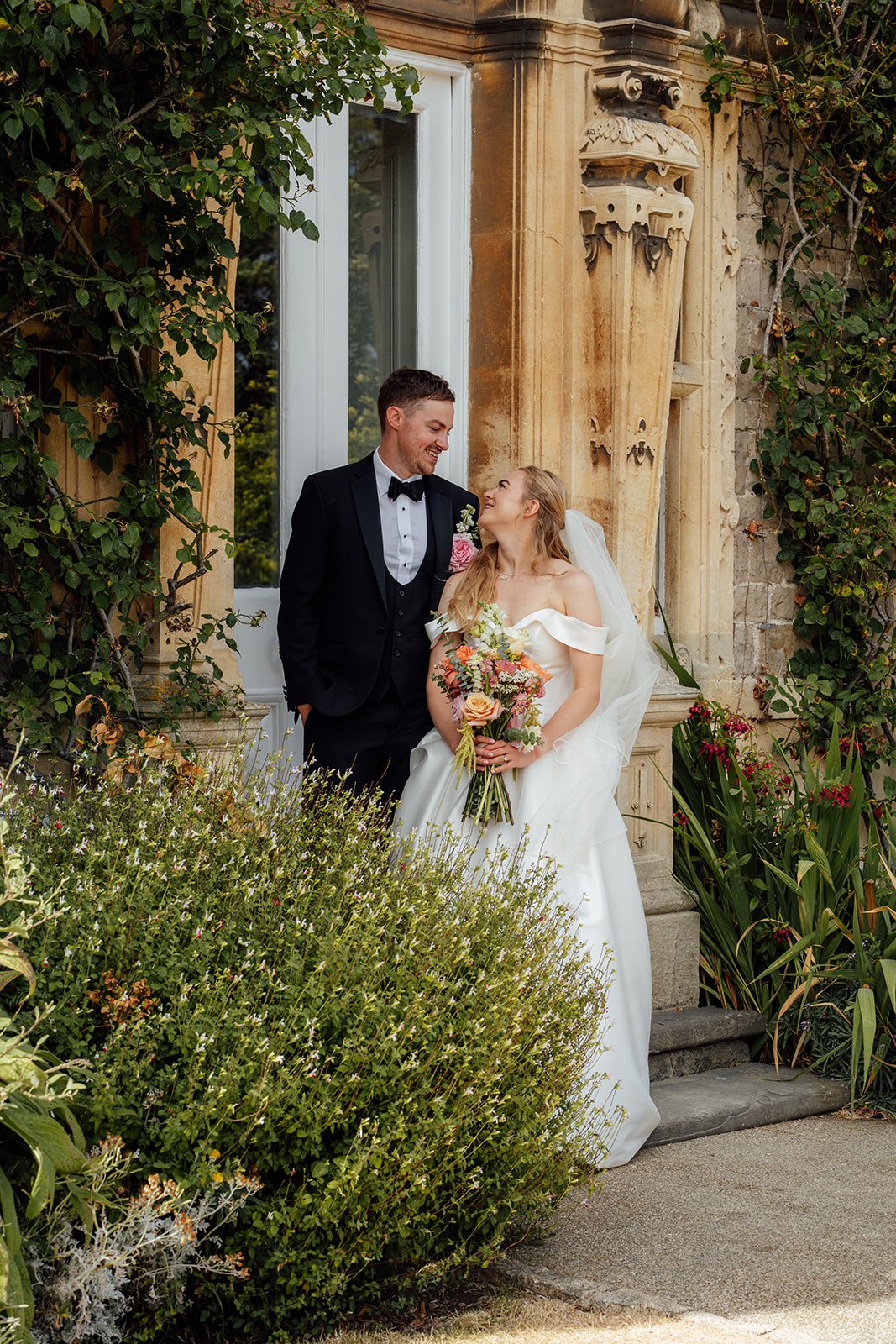 Caitlin and Kevin sharing a quiet moment beside the ivy-covered stonework at Clevedon Hall in Somerset, with Caitlin holding her colourful bridal bouquet.