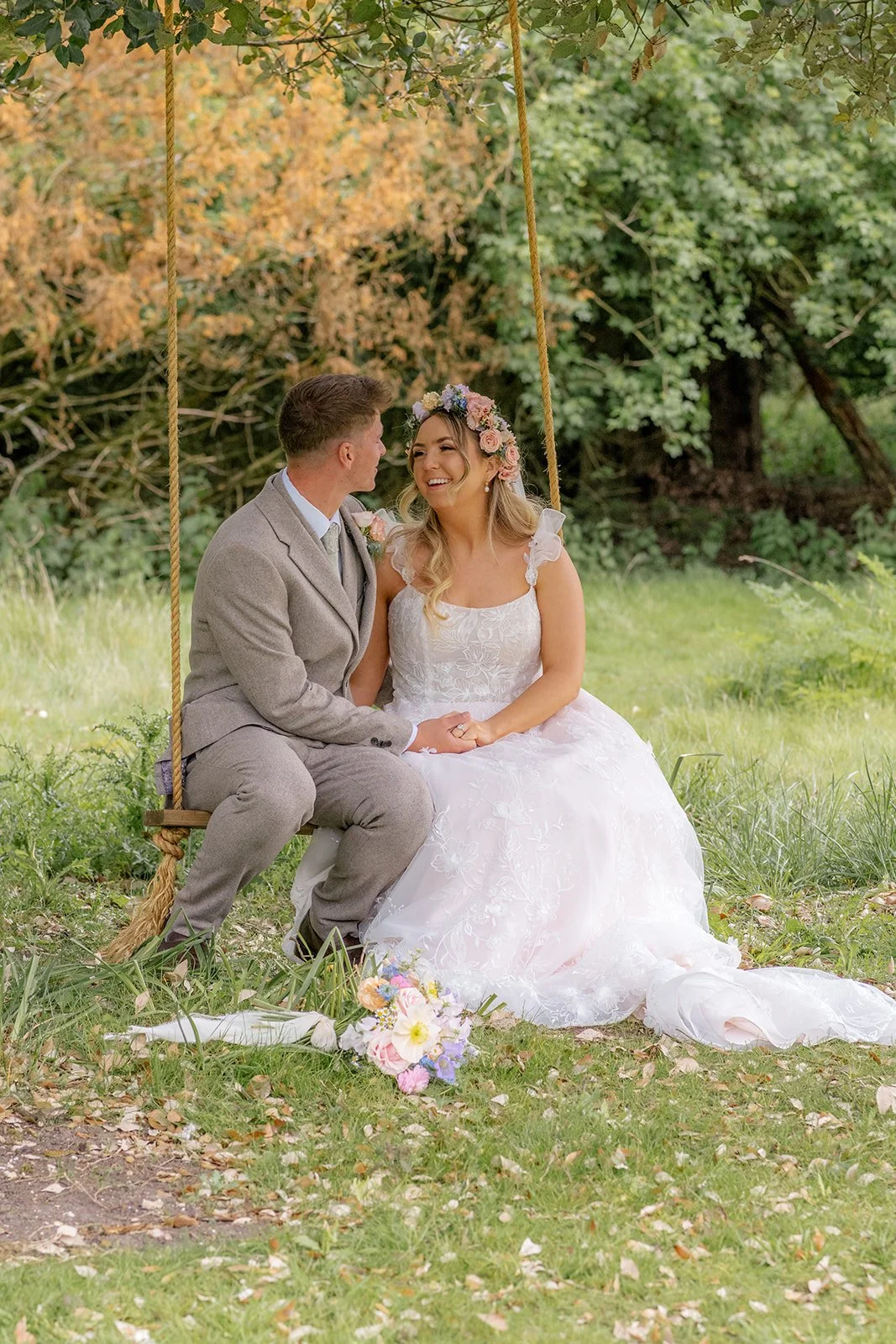 Jaye & Josh sitting together on a garden swing at Syrencot in Wiltshire, smiling beneath the trees, photographed by Just James Weddings for relaxed outdoor wedding portraits.