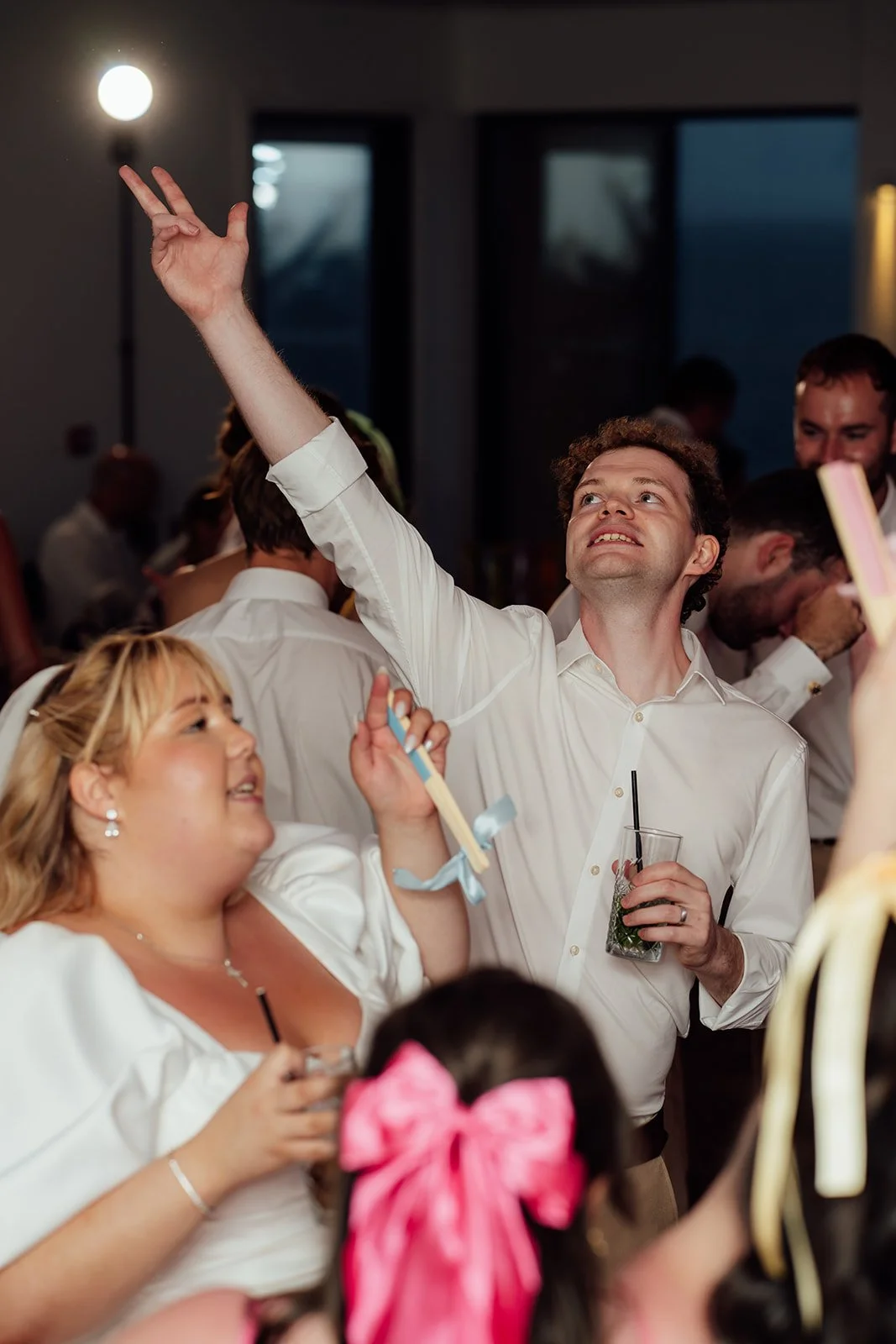 Alex raises one hand while dancing beside Holly and wedding guests during the lively evening reception at Sandy Cove Hotel in North Devon, photographed by Just James Weddings.