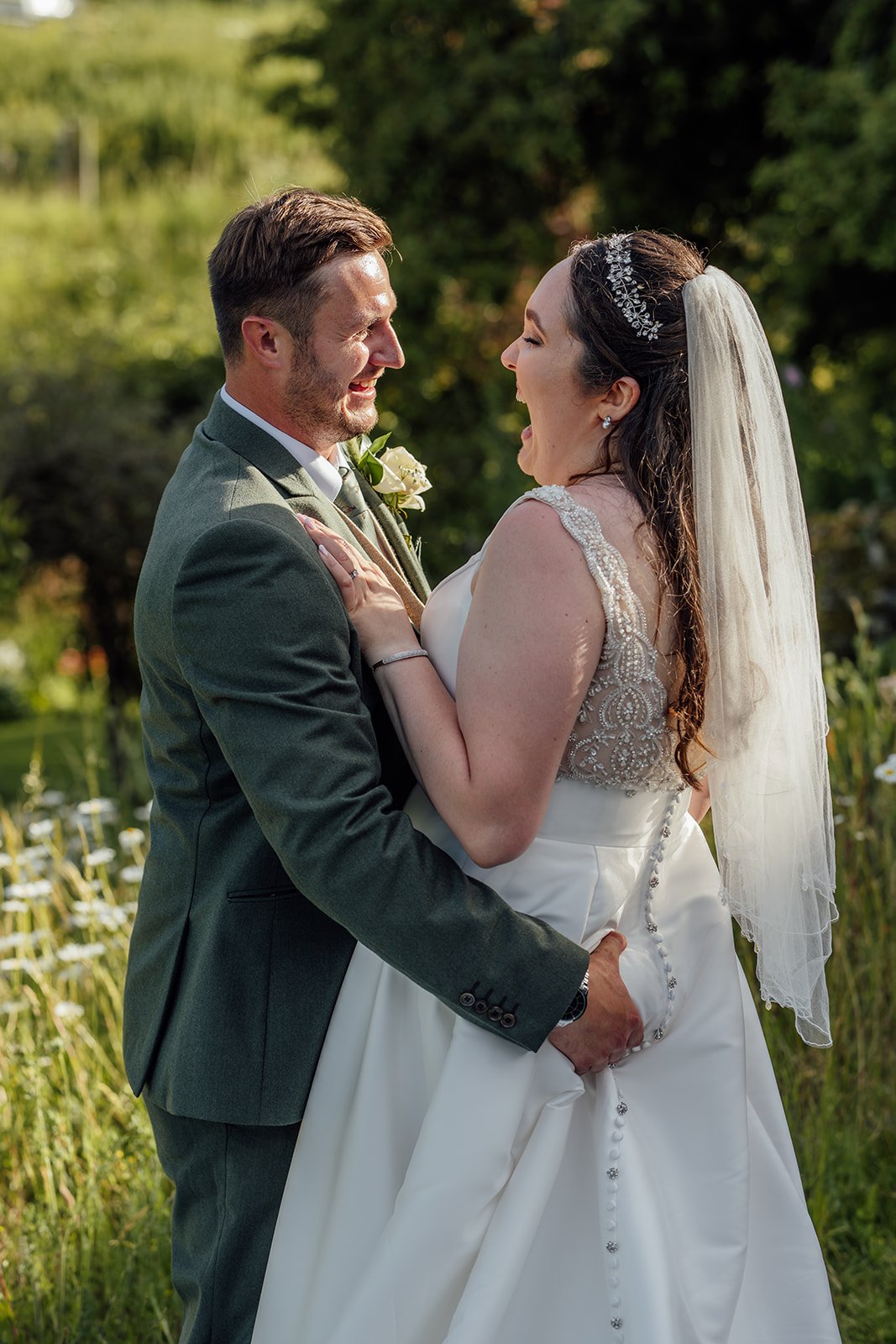 Chloe & Armani laughing together outdoors at The Barn at Upcote in the Cotswolds, photographed by Just James Weddings for relaxed natural wedding portraits.