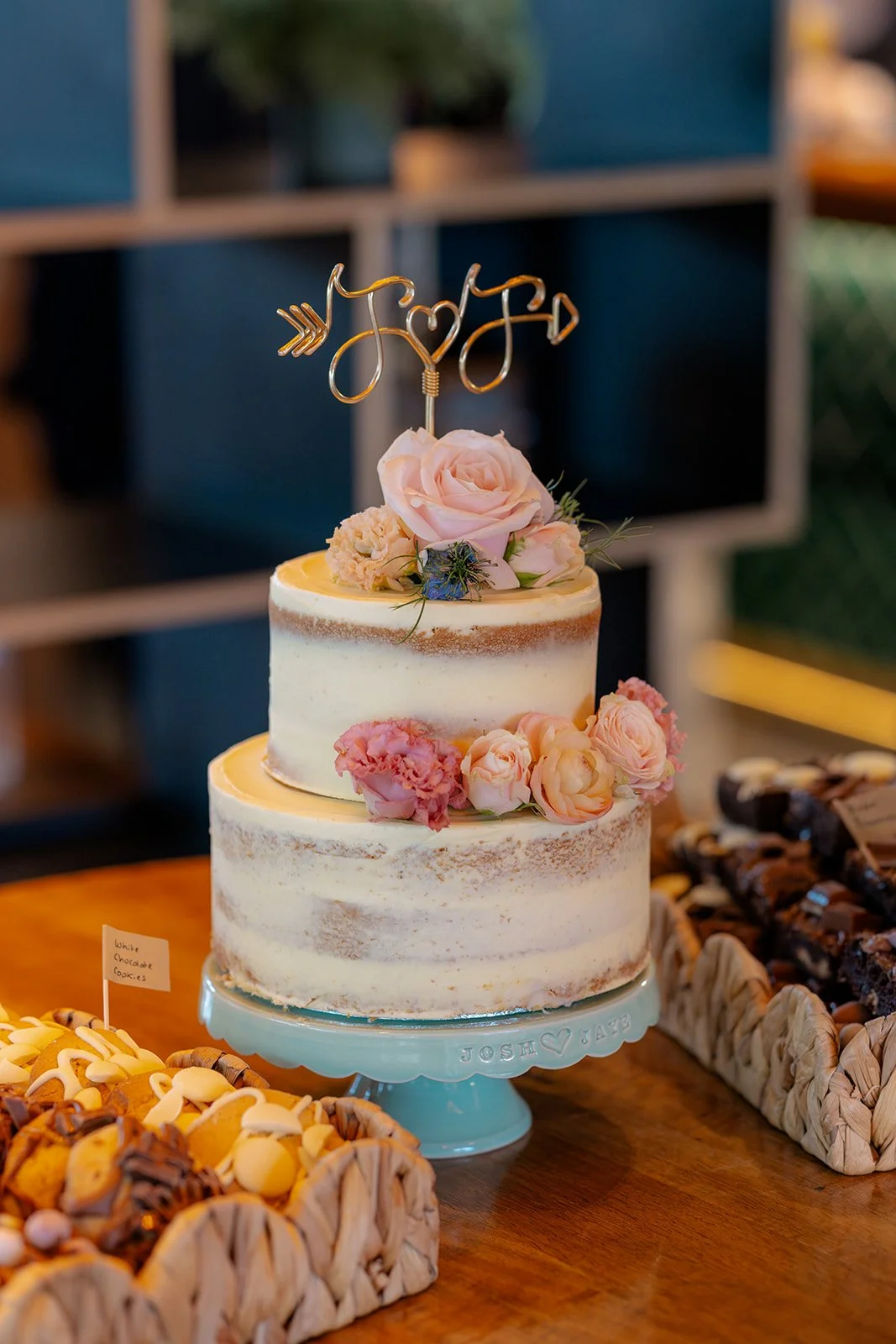 Two-tier wedding cake at Syrencot in Wiltshire, decorated with pink flowers and a personalised topper, photographed by Just James Weddings for colourful wedding reception details.