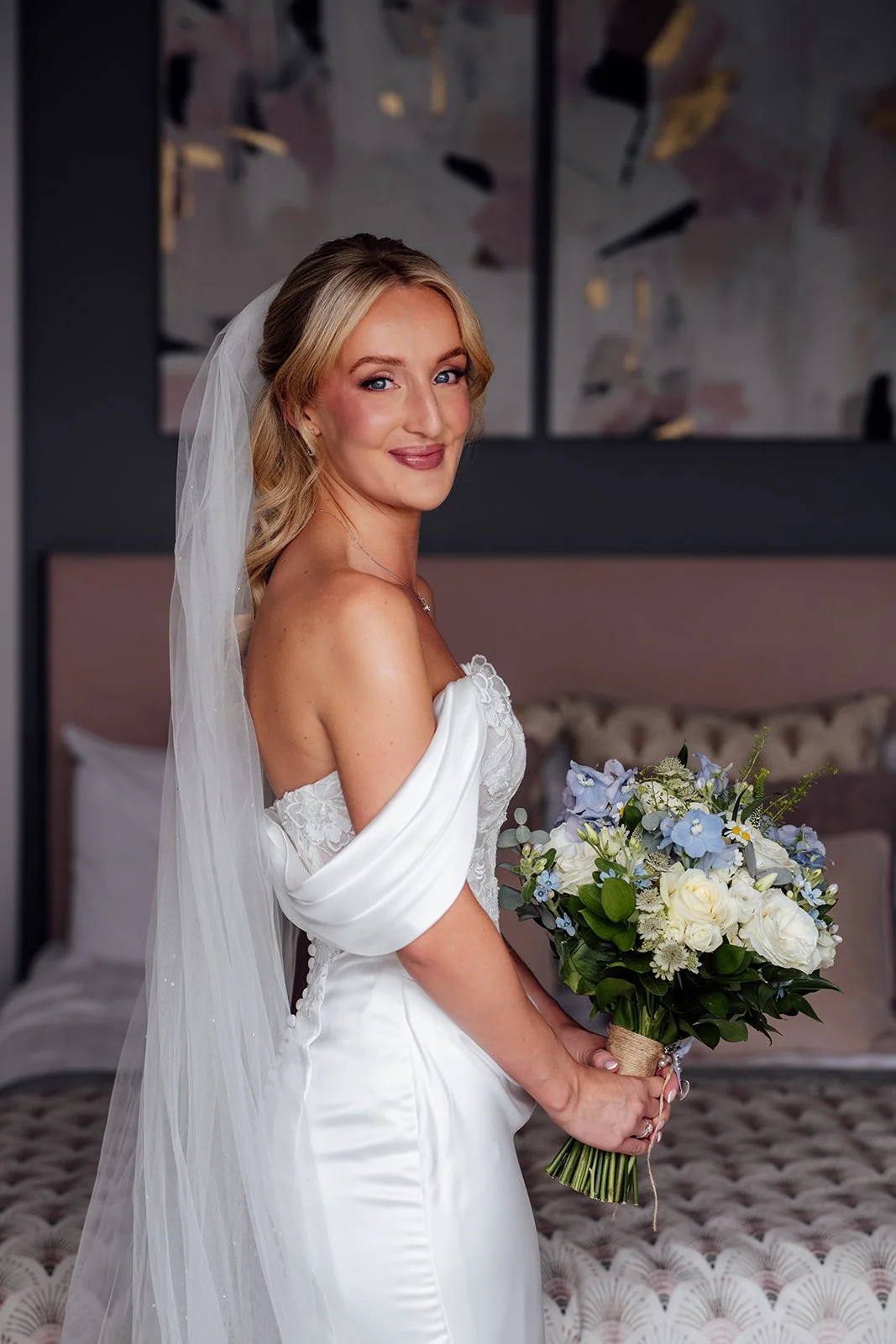 Bridal portrait of Amy wearing her veil and fitted wedding dress while holding a bouquet of white roses and blue flowers at Sandy Cove Hotel in North Devon, UK.