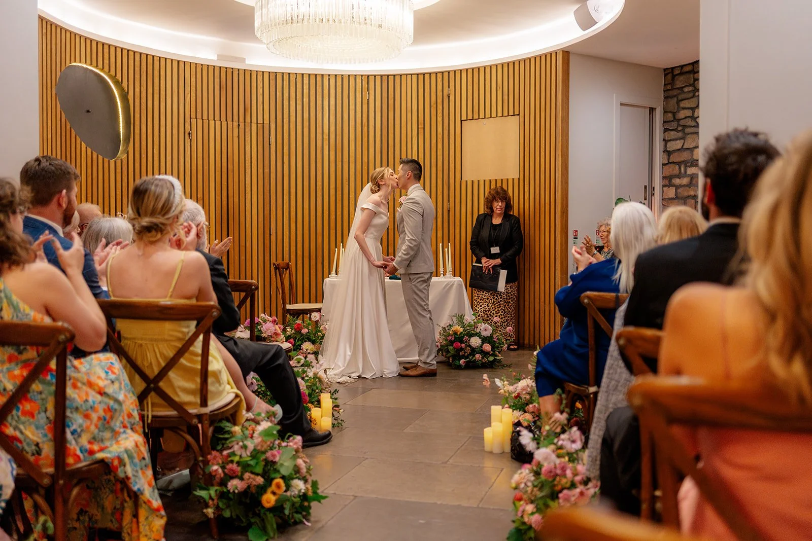Brian & Josie sharing their first kiss during their indoor ceremony at Clifton Observatory in Somerset, surrounded by guests and flowers, photographed by Just James Weddings.