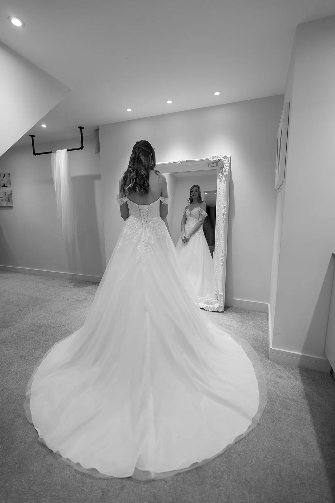 Bride Hannah standing in her wedding dress before a mirror during bridal preparations for Hannah & Cameron’s wedding at Sandy Cove Hotel, North Devon. Black and white portrait capturing a quiet moment before coastal wedding ceremony begins.