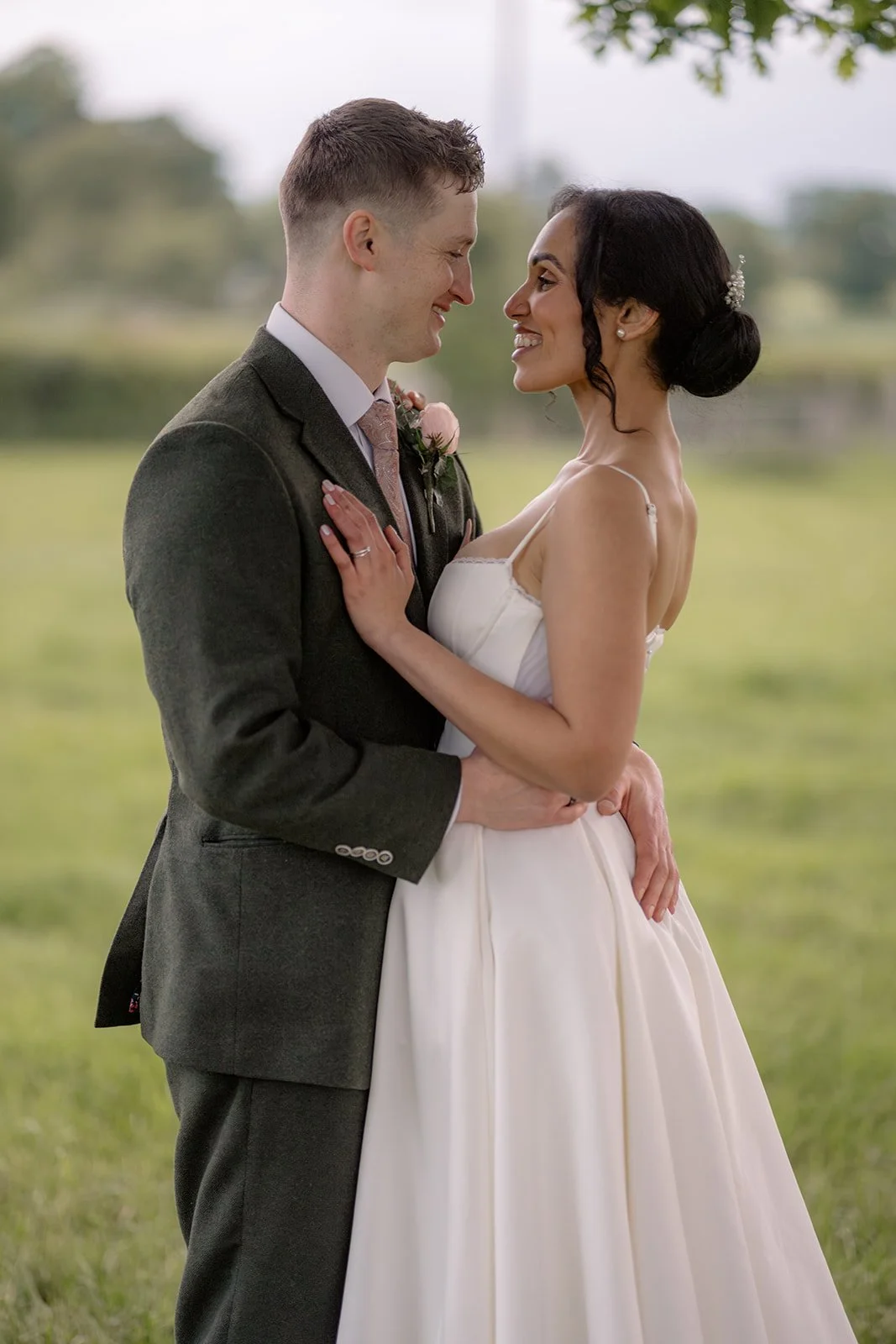 Jaye & Josh share a soft countryside portrait at Farrington's Farm in Bristol, smiling close together in the fields after their wedding, with the groom in a green suit, the bride in a simple white dress and gentle summer greenery behind them.