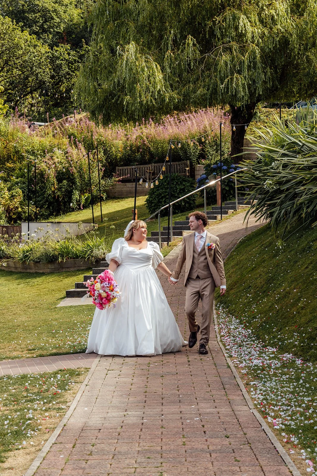 Holly & Alex walk hand in hand through the gardens after their ceremony at Sandy Cove Hotel in North Devon, photographed by Just James Weddings.