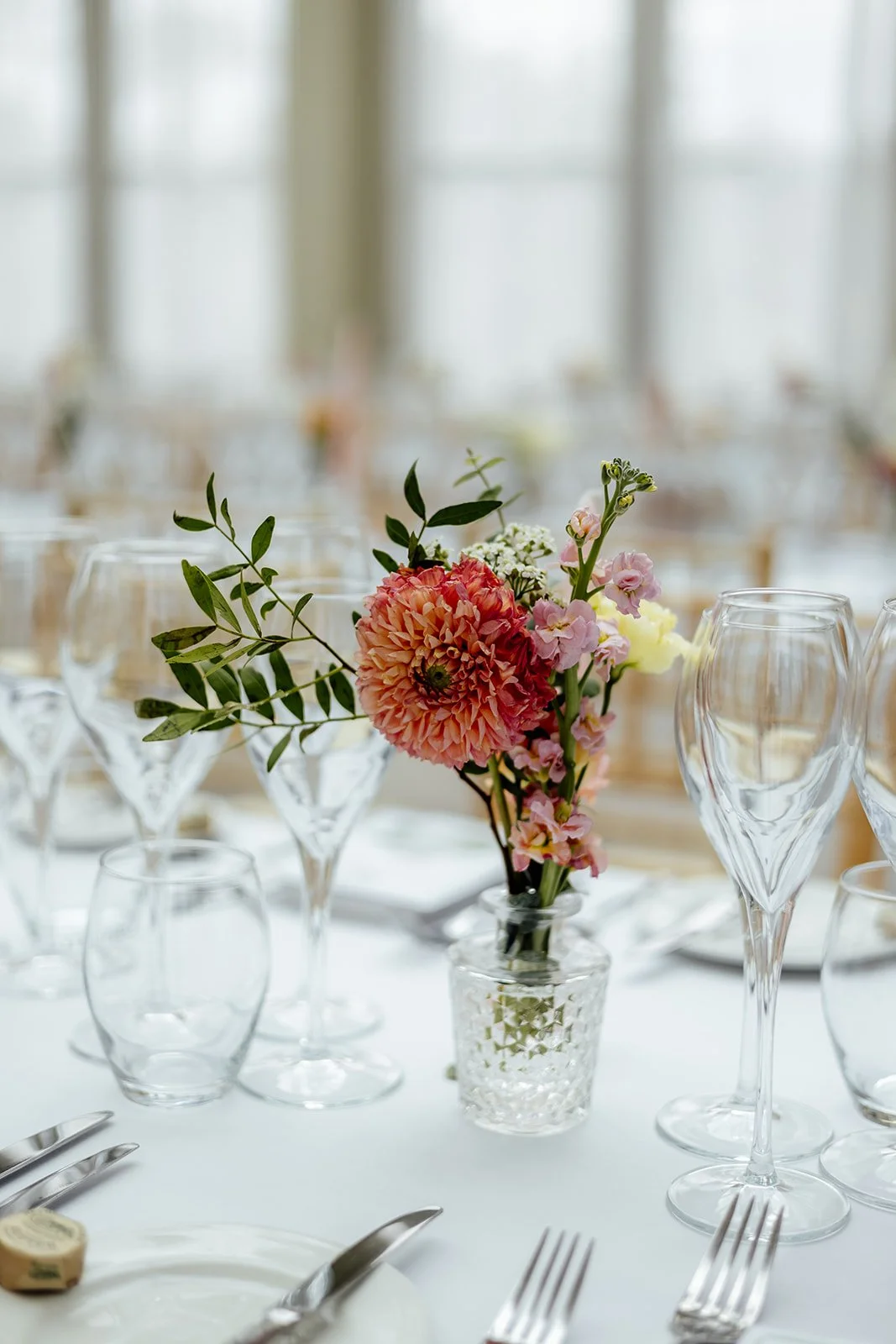 Close up of a colourful floral centrepiece at Caitlin & Kevin’s wedding at Clevedon Hall in Somerset, surrounded by glassware and table settings, photographed by Just James Weddings.