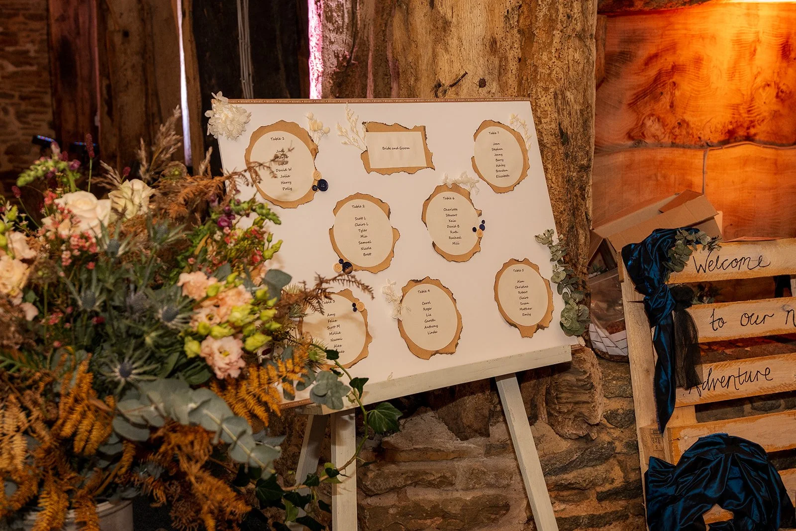 Autumn wedding table plan at Stockbridge Farm Barn in Dorset, displayed on an easel beside seasonal flowers, dried foliage and rustic wooden signs, photographed by Just James Weddings.