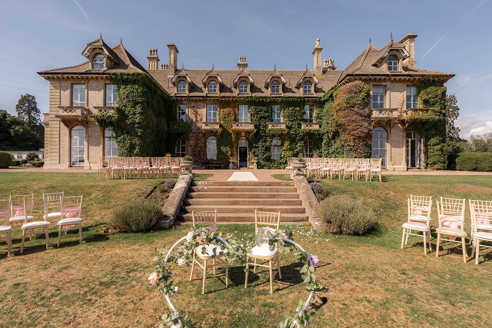Outdoor ceremony setup at Eastwood Park in Gloucestershire, with the manor house, aisle chairs and floral styling, photographed by Just James Weddings for elegant wedding venue inspiration.