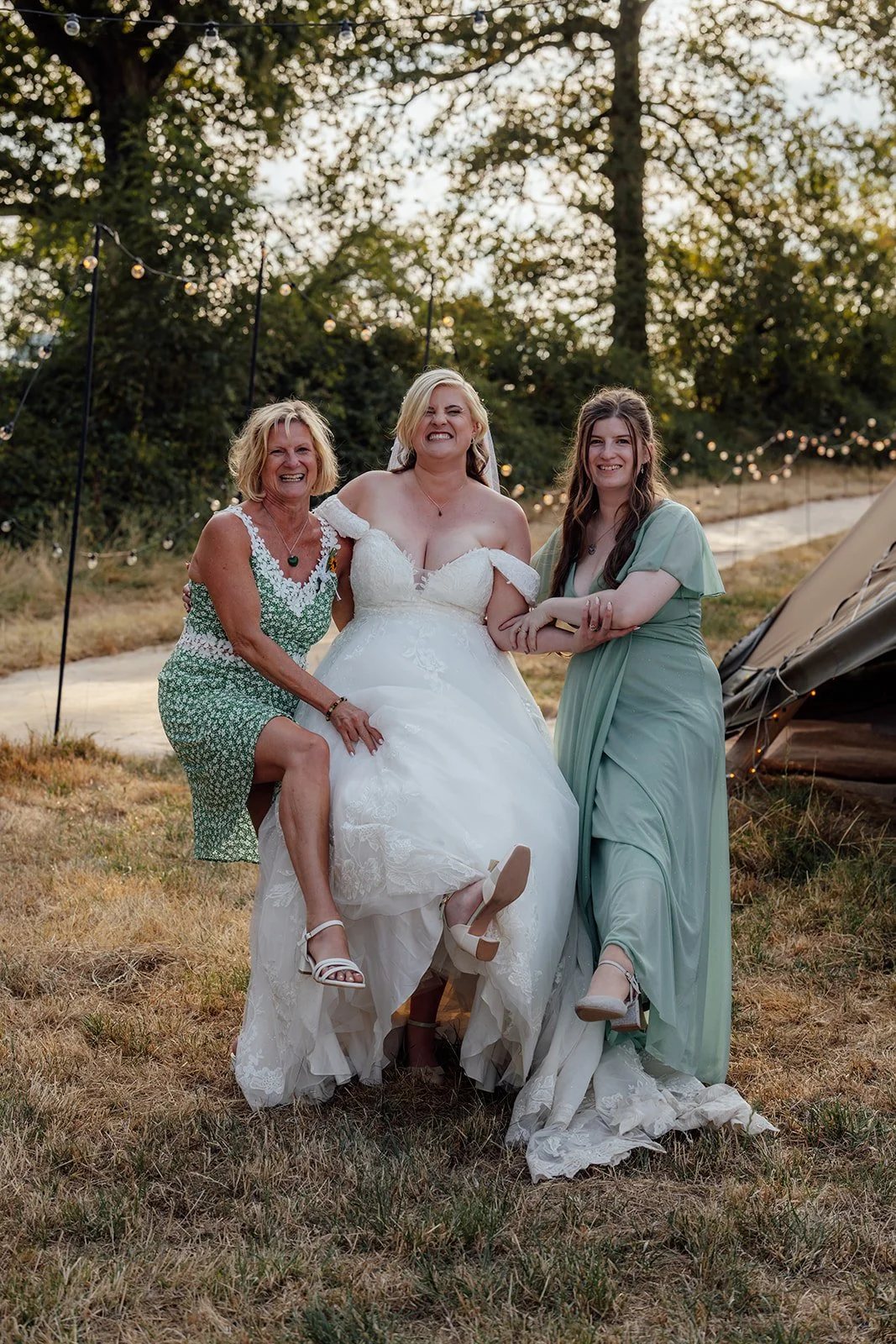 Lucy laughing with two wedding guests during a fun outdoor portrait near the tipi reception at Curated Canvas at Noah’s Pond in Somerset, photographed by Just James Weddings.