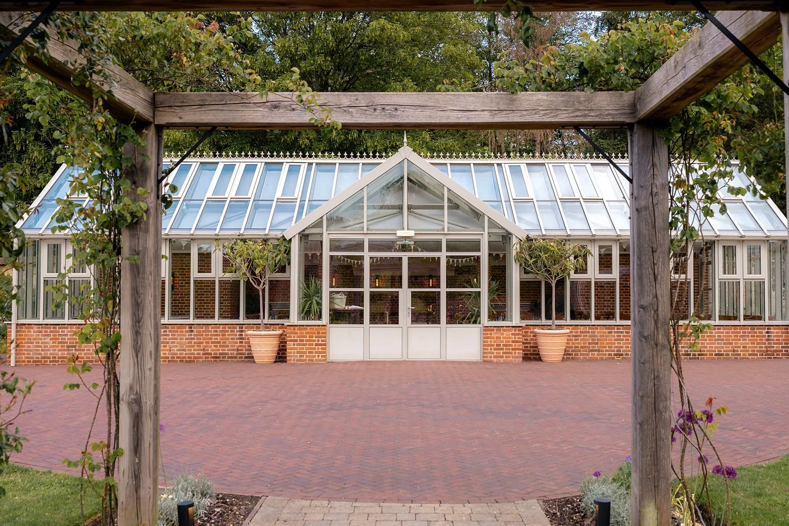 Exterior view of the ceremony building at Syrencot in Wiltshire, framed by a wooden pergola and garden greenery, photographed by Just James Weddings for wedding venue inspiration.