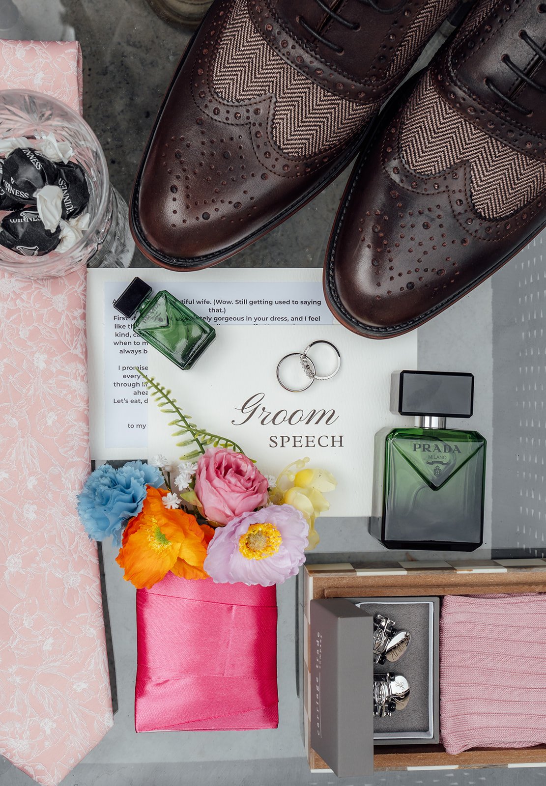 Flat lay of Alex’s wedding details with brown brogue shoes, rings, Prada fragrance, cufflinks, flowers and groom’s speech at Sandy Cove Hotel in North Devon, photographed by Just James Weddings.