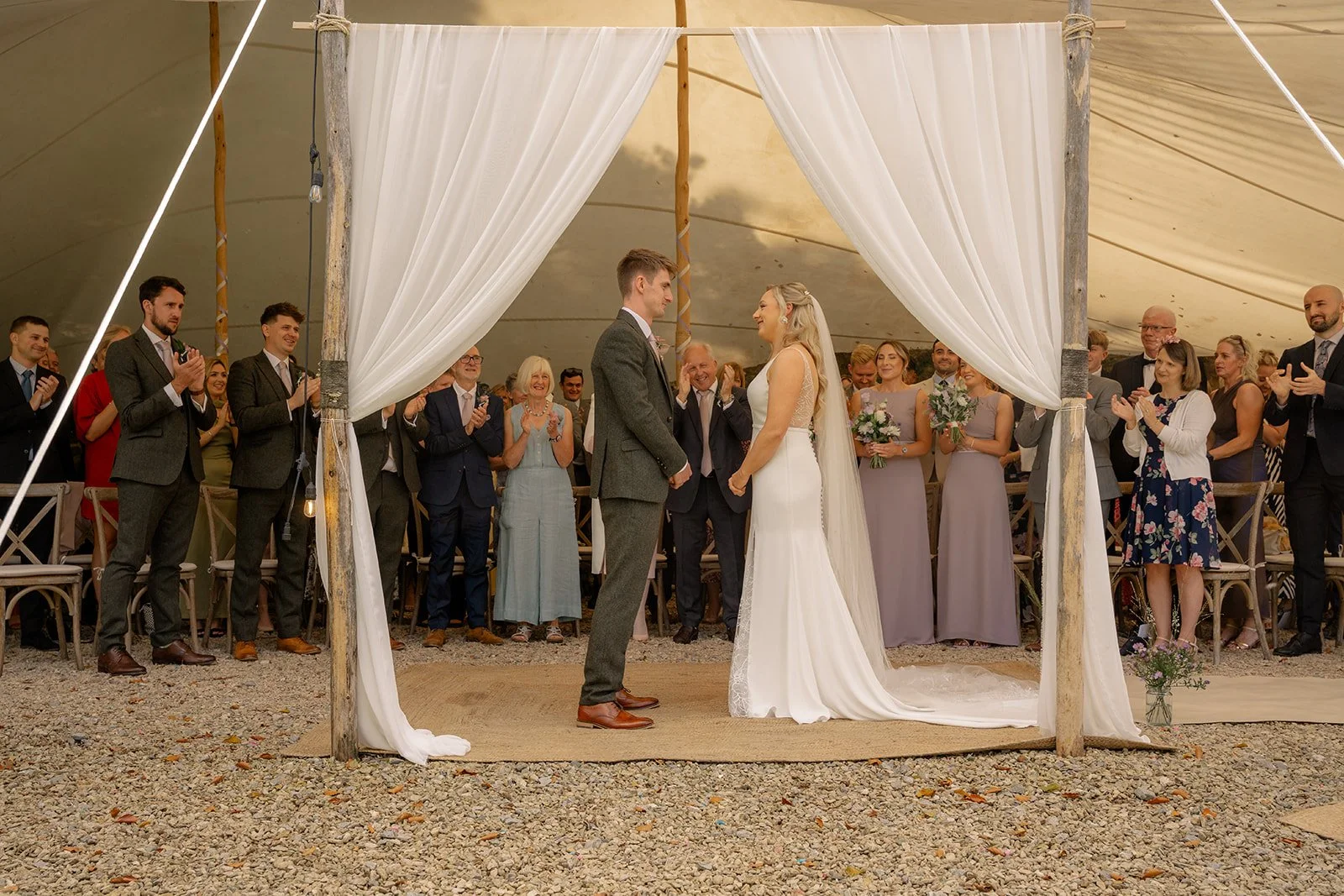 Abi & Josh standing under white drapes during their outdoor ceremony at The Cider Barn in Somerset, photographed by Just James Weddings for relaxed countryside wedding ceremony moments.