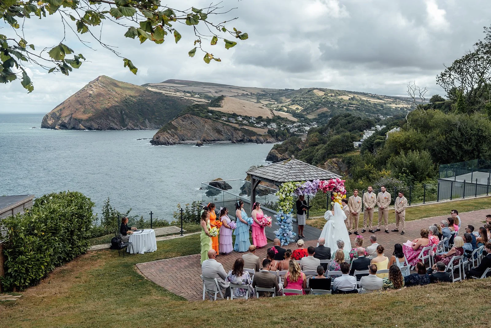 Wide view of Holly & Alex’s outdoor wedding ceremony overlooking the dramatic North Devon coastline at Sandy Cove Hotel, photographed by Just James Weddings.