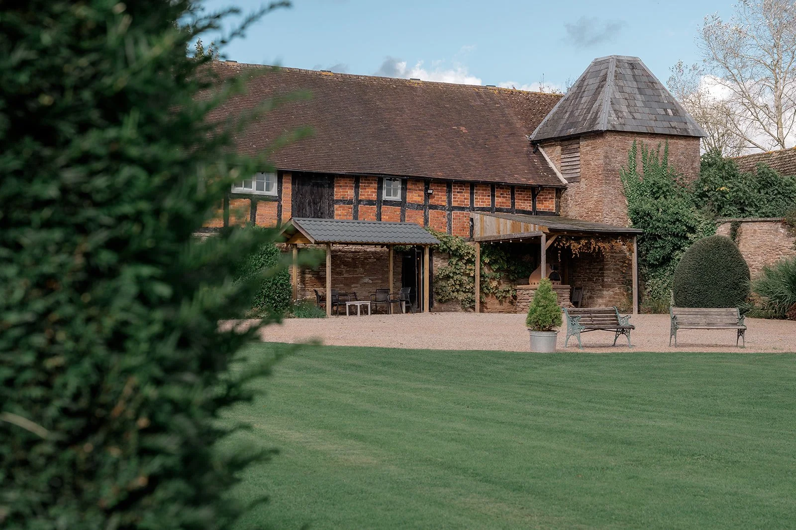 Exterior view of the rustic timber and brick outbuildings at Broadfield Court in Herefordshire, overlooking the lawn and courtyard, photographed by Just James Weddings for venue inspiration.
