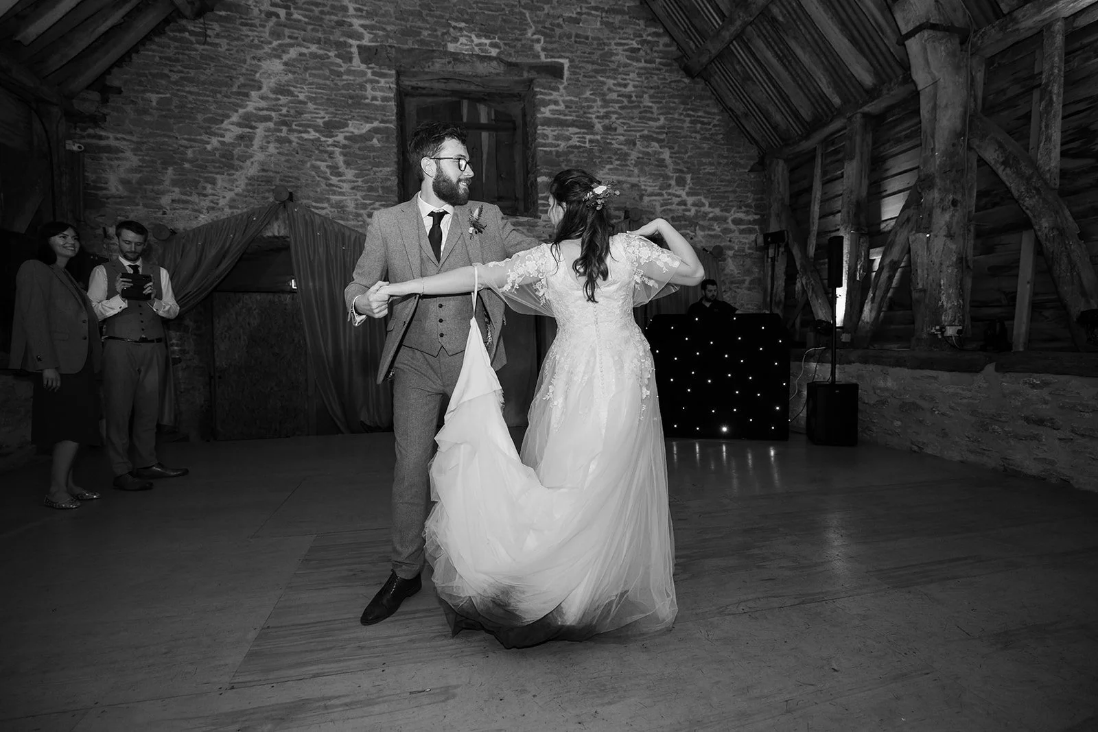 Black and white photo of Maisie & Andrew dancing together inside Stockbridge Farm Barn in Dorset, photographed by Just James Weddings for lively autumn wedding reception moments.