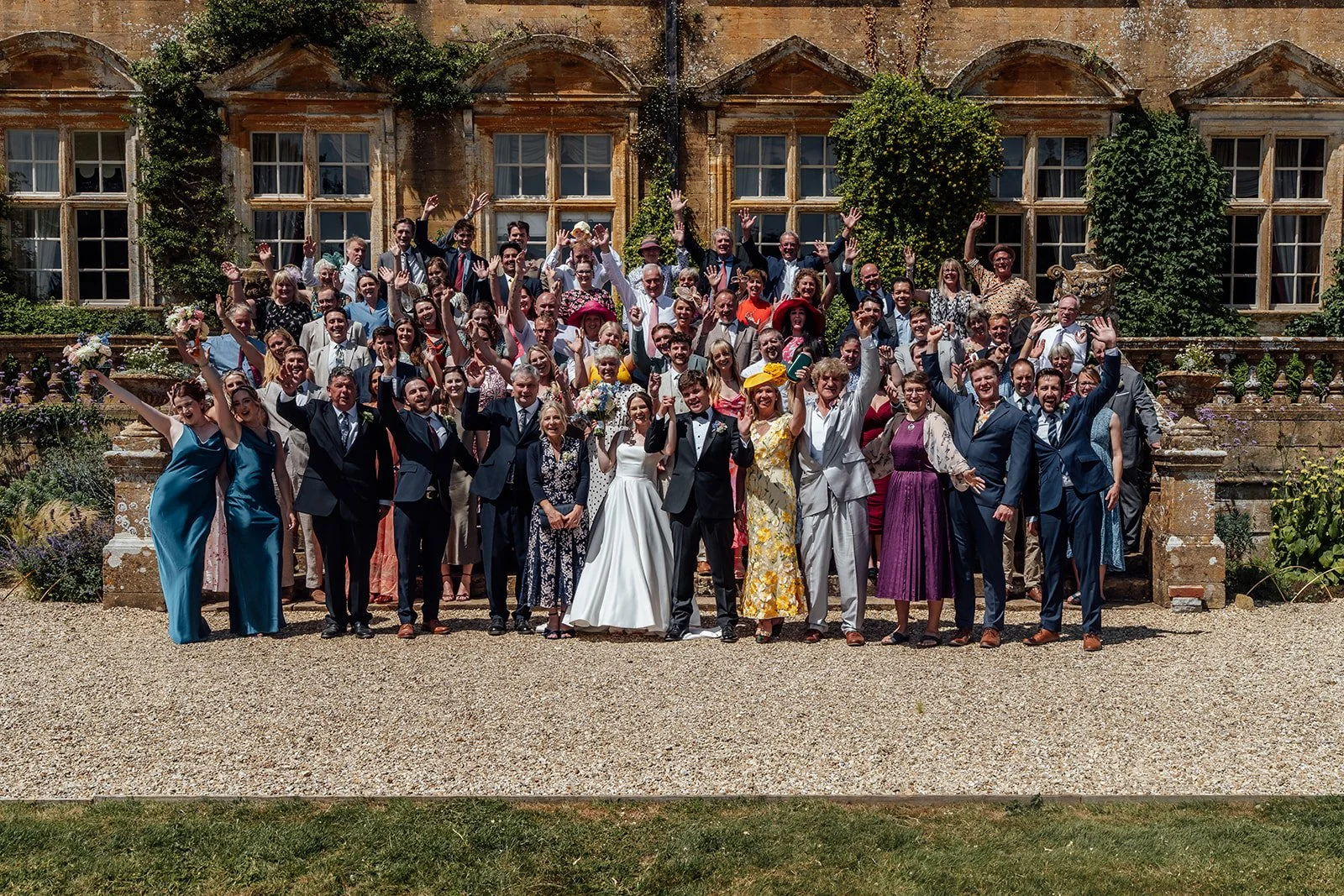 Rachel & Tom stand at the centre of a large group photo with their wedding guests outside the historic Brympton House in Somerset, photographed by Just James Weddings.