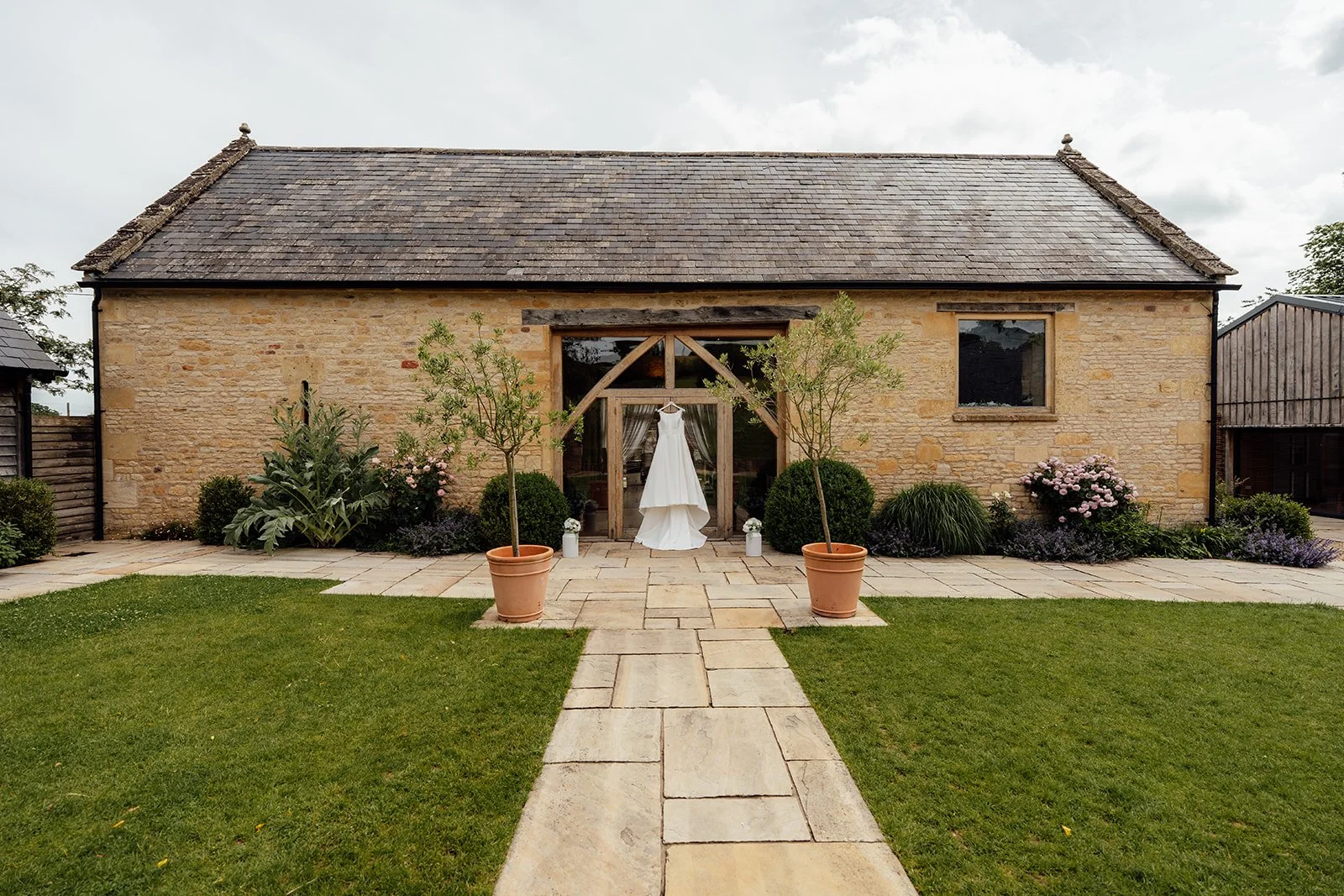 Chloe and Armani’s wedding dress displayed outside the stone barn and landscaped gardens at The Barn at Upcote in Gloucestershire, photographed by Just James Weddings.