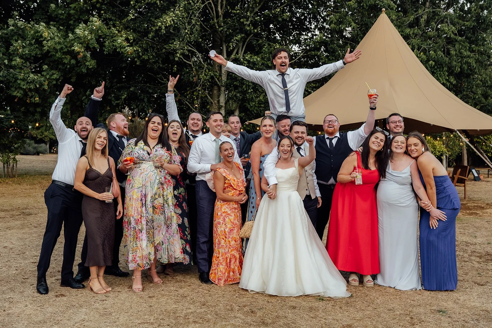 Harriet & Simon pose with a large group of friends outside the tipi during their evening celebrations at Dovecote Events in Oxfordshire, photographed by Just James Weddings.