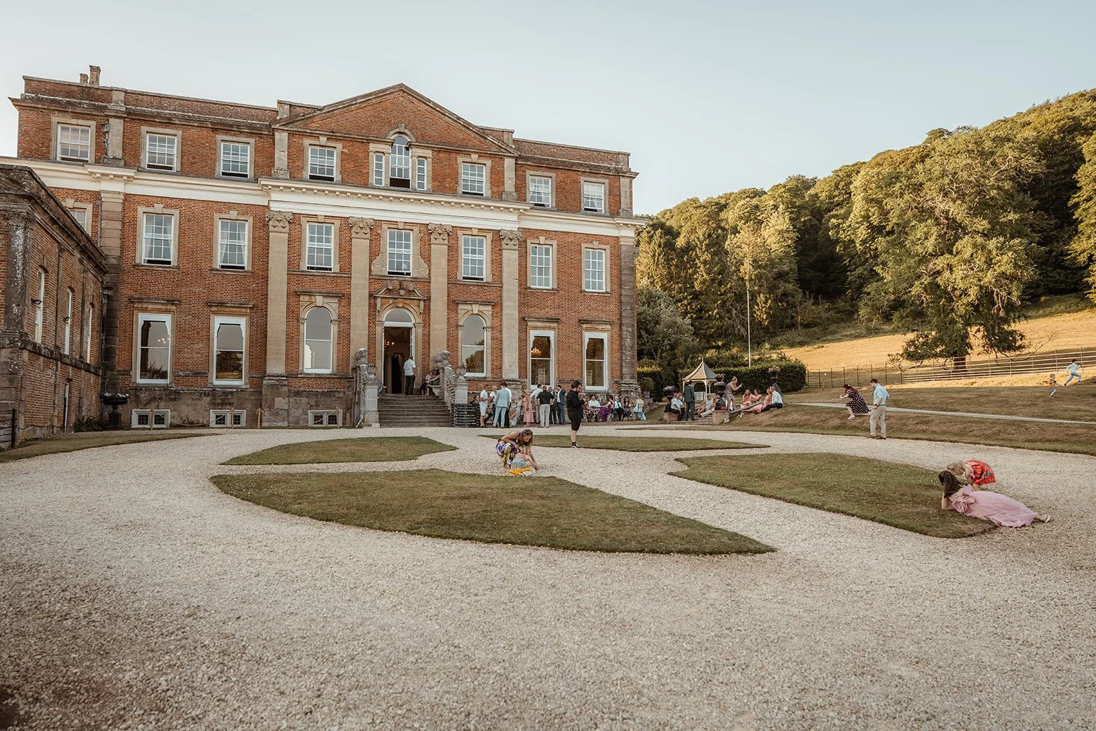 Guests relax outside Crowcombe Court in Somerset, UK, during Michelle and Andy’s wedding reception, with the grand country house and surrounding Somerset countryside in view.