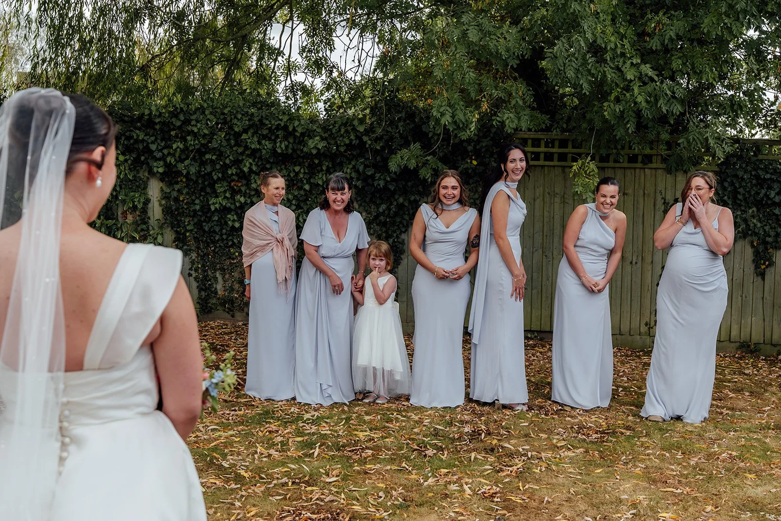 Harriet’s bridesmaids react with smiles and laughter as they see her in her wedding dress before the ceremony at Dovecote Events in Oxfordshire, photographed by Just James Weddings.