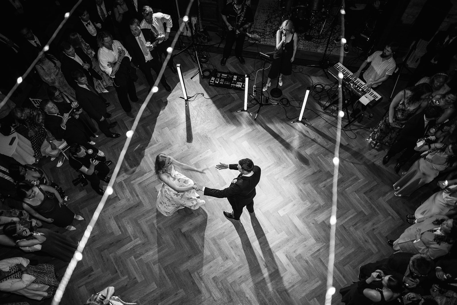 Black and white overhead photo of Caitlin & Kevin dancing together at Clevedon Hall in Somerset, surrounded by guests and hanging lights, photographed by Just James Weddings for lively evening wedding moments.
