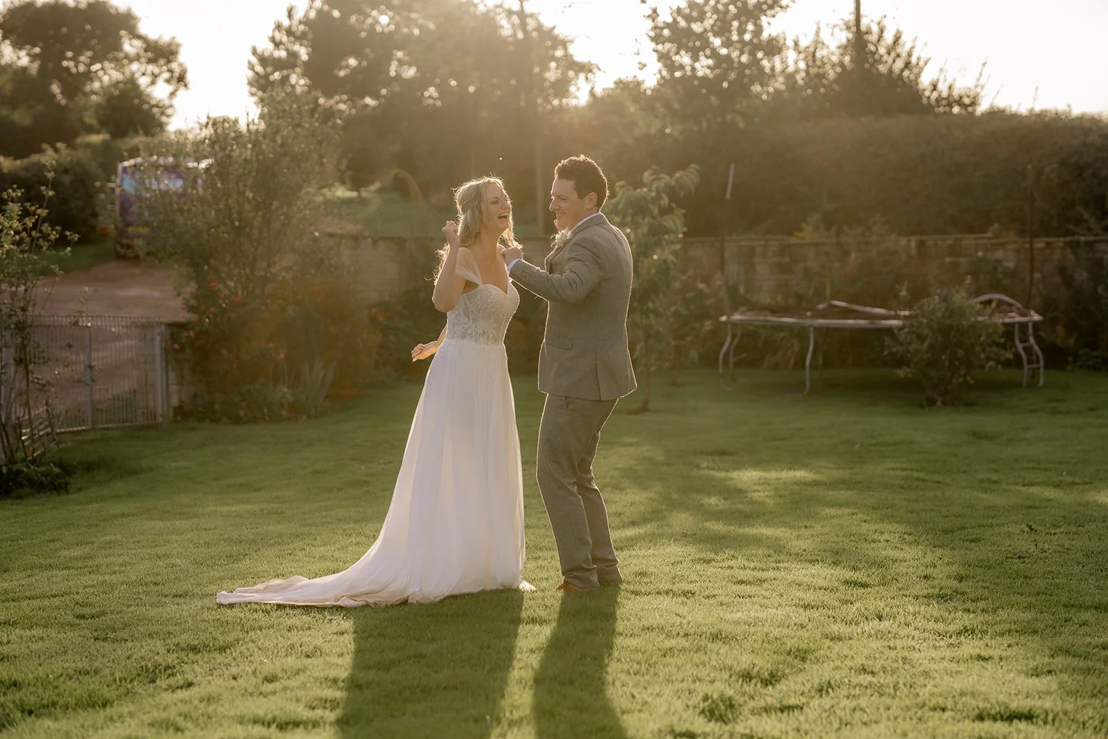Samantha and Mike laugh and dance together on the lawn, facing each other as warm evening light falls around them. Their relaxed movement and expressions capture a joyful, carefree moment during their outdoor wedding portraits.