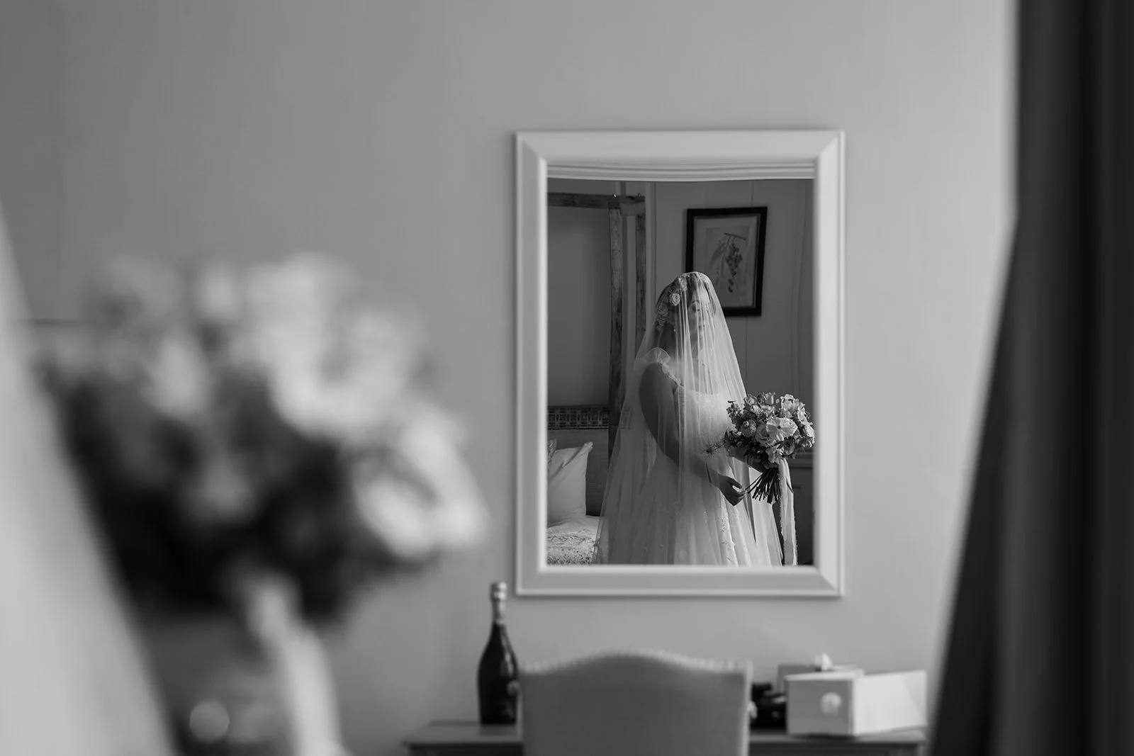 Black and white bridal preparation photo of Jaye reflected in a mirror at Syrencot in Wiltshire, holding her bouquet before the ceremony, photographed by Just James Weddings.