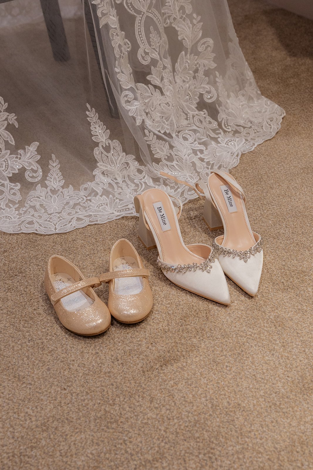 Bridal detail from Andrew & Daisy’s Sandy Cove Hotel wedding in Devon, featuring ivory Be Mine heels with crystal trim beside glitter flower girl shoes on carpet beneath Daisy’s lace wedding dress train.