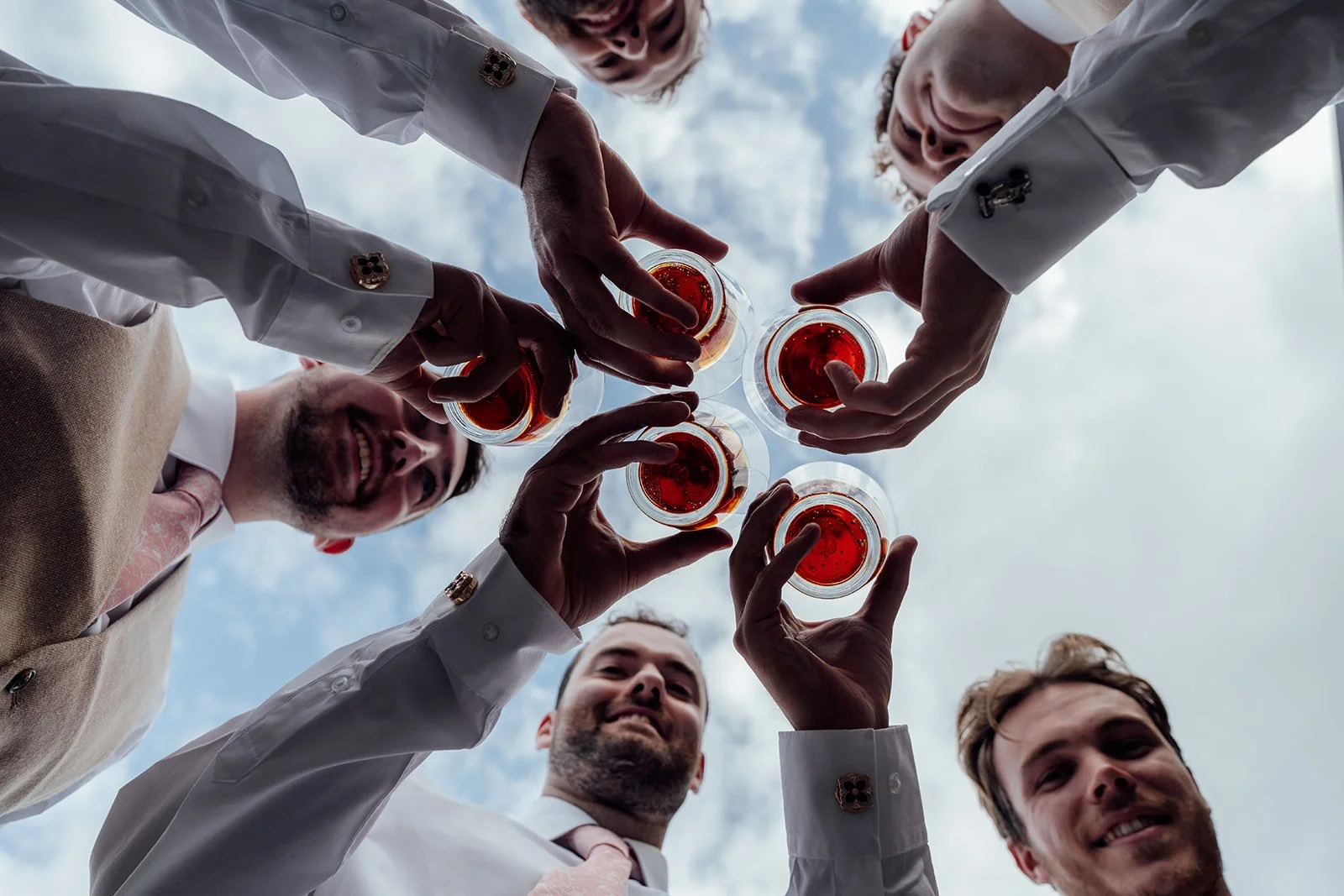 Alex and his groomsmen raise glasses together in a playful low-angle wedding photo at Sandy Cove Hotel in North Devon, photographed by Just James Weddings.