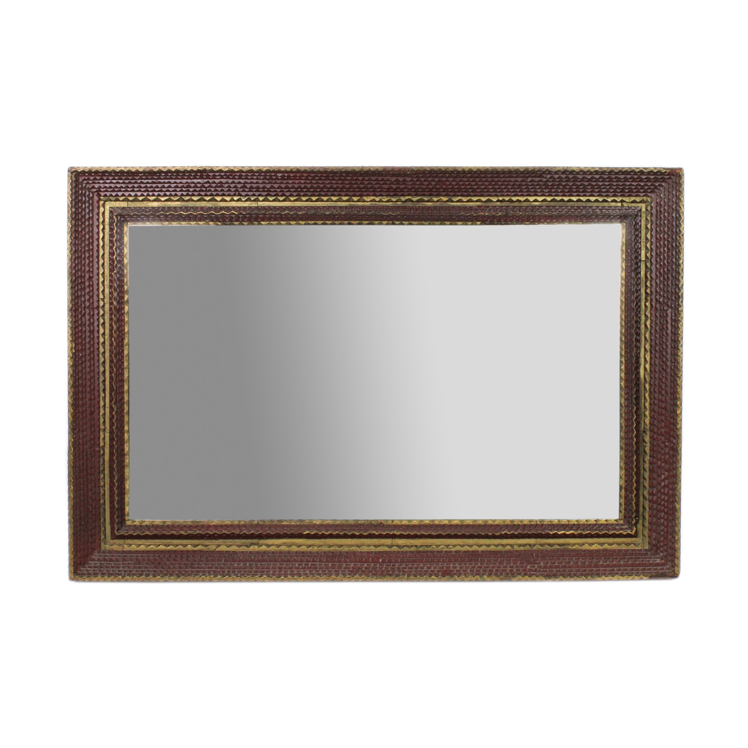 An ornately-carved, rectangular wood frame around a mirror. The carvings are small triangles like rows of teeth all around the mirror. Rows are painted a brown color with stripes of gold interspersed.