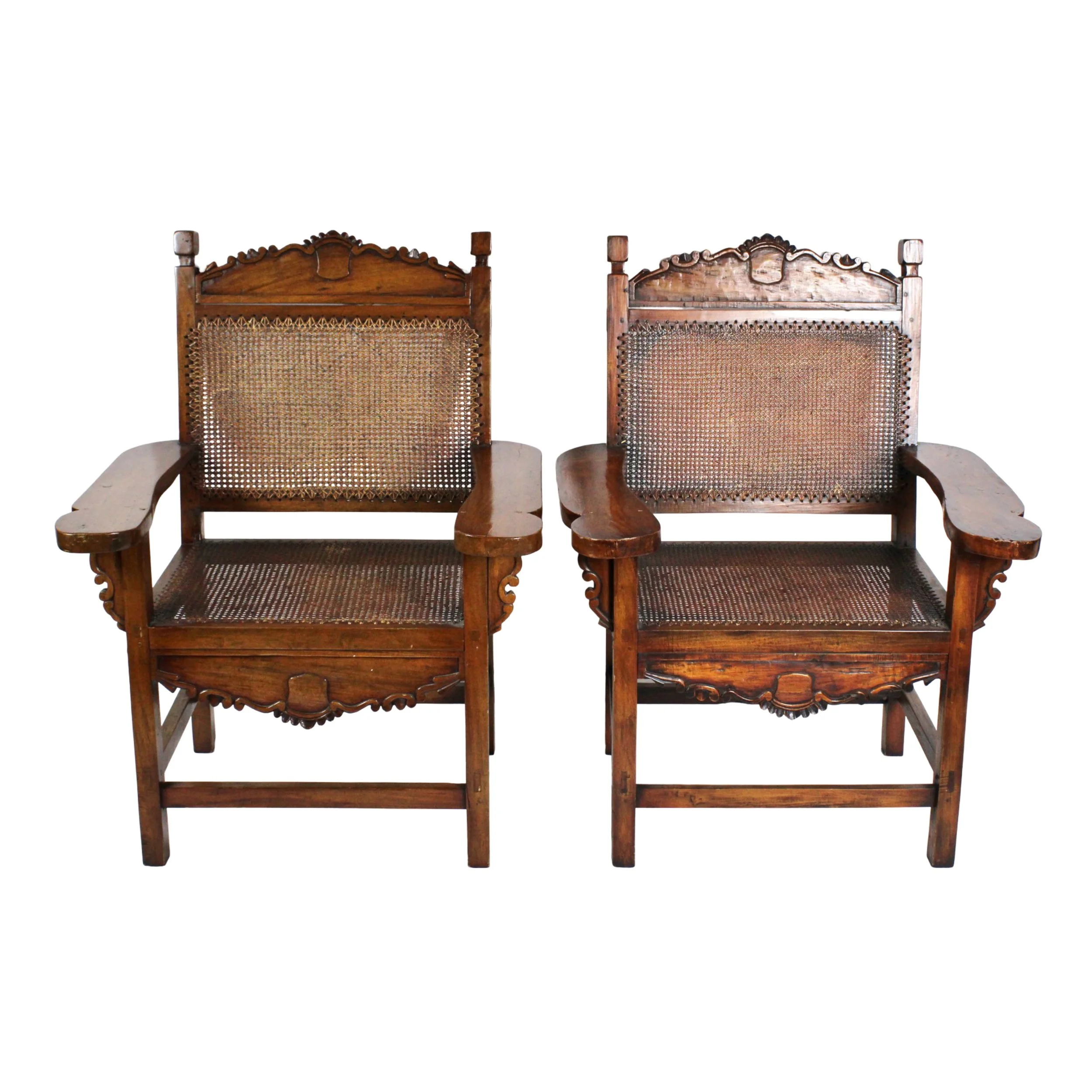Pair of matching large carved dark wood chairs, with woven caned backs and seats. Intricate hand carved details along the top edge of the back and apron below the seats, with wide wood arms
