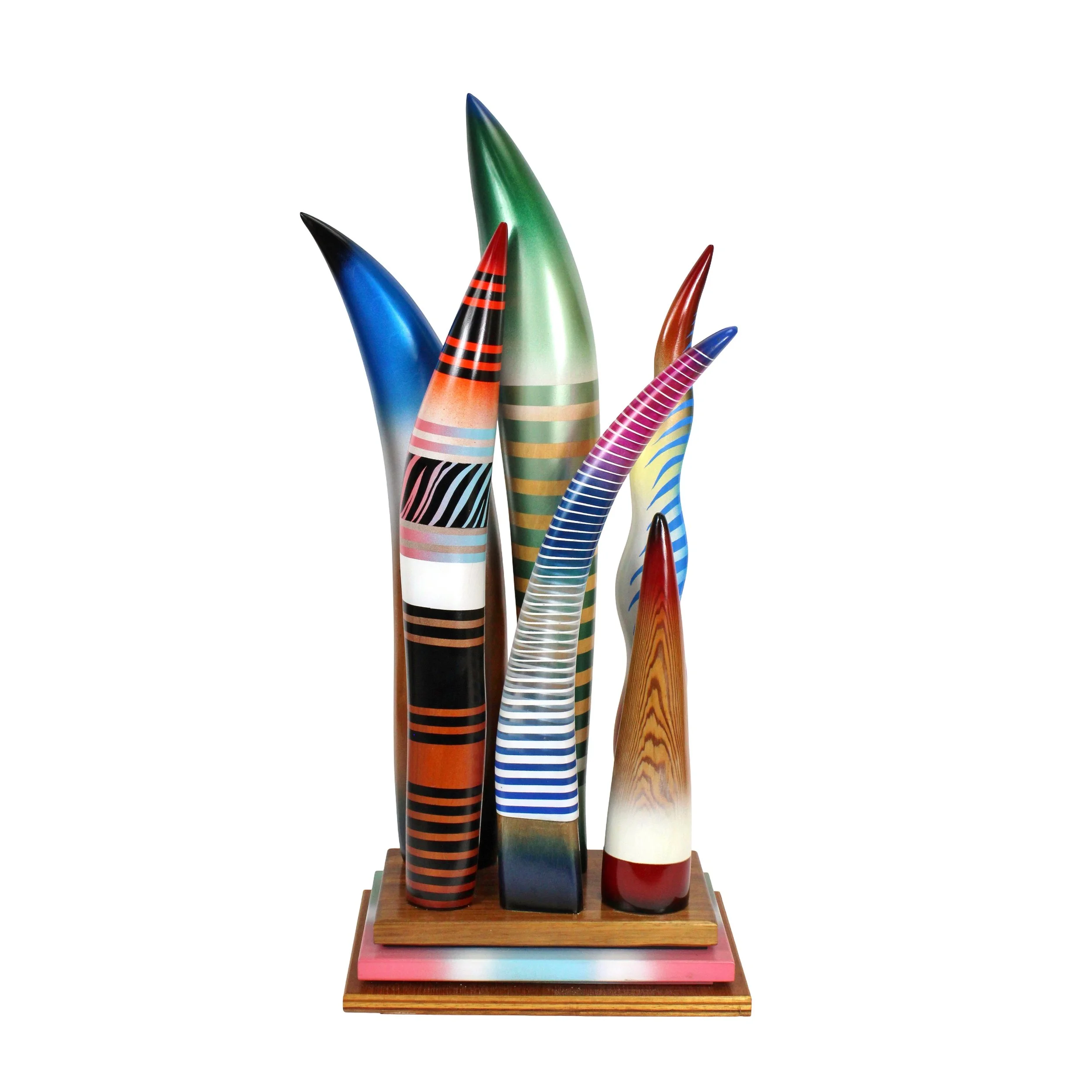Tall modern sculpture with two rows of three grass blade shaped colorful sections, mounted to a tiered platform base. Includes stripes and gradients of blue, orange, black, white, pink, red, and green