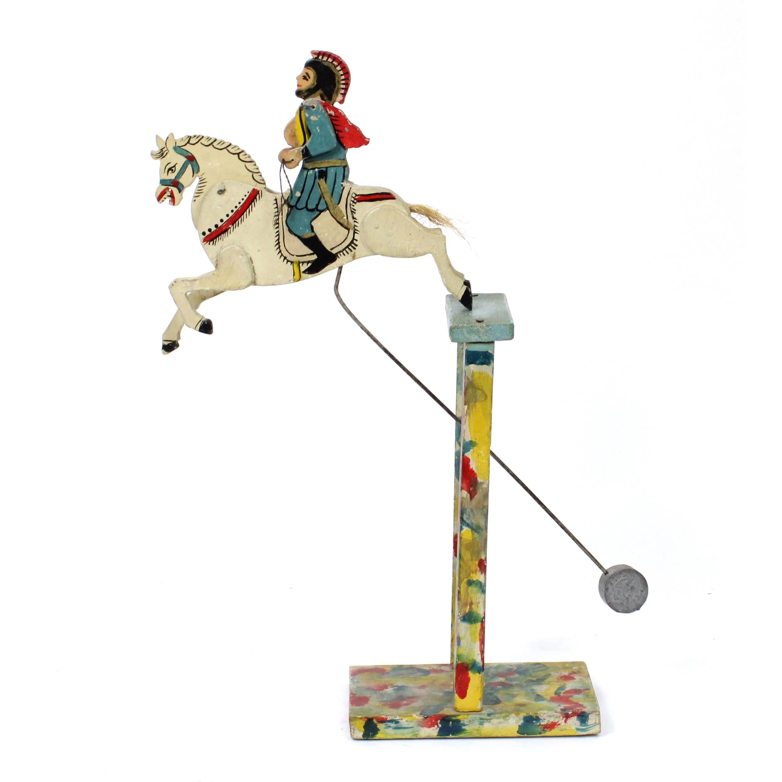 Painted wood sculpture of soldier in Greek or Roman armor riding a white horse perched on a wood base. The soldier's red, blue, and yellow accents are mirrored in the dappled paint on the base.