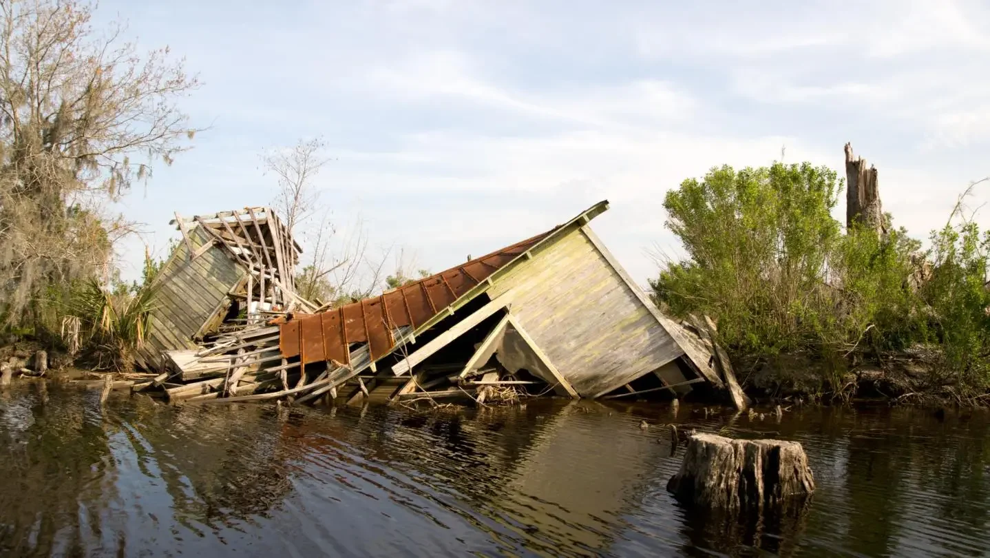 Flooded area with a partially collapsed wooden building and trees on the water's edge