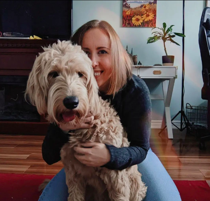 A woman hugging a large, fluffy tan dog in a room with a modern desk, a plant, and a painting on the wall.